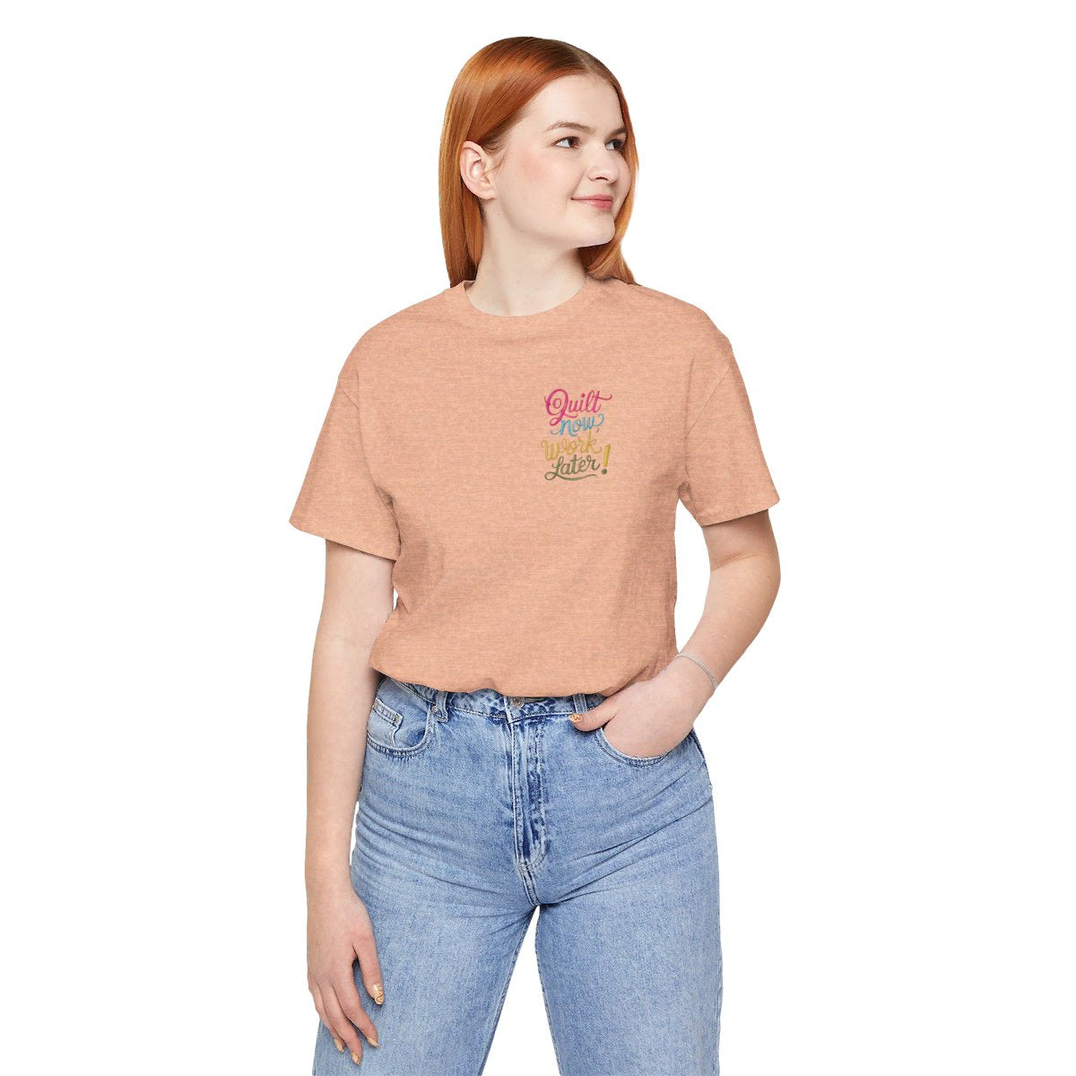 A Heather Peach funny quilting T-shirt featuring bold, stylized text that reads "Quilt Now, Work Later" in various vibrant colors. The playful design captures the spirit of passionate quilters who prioritize their craft over other responsibilities.