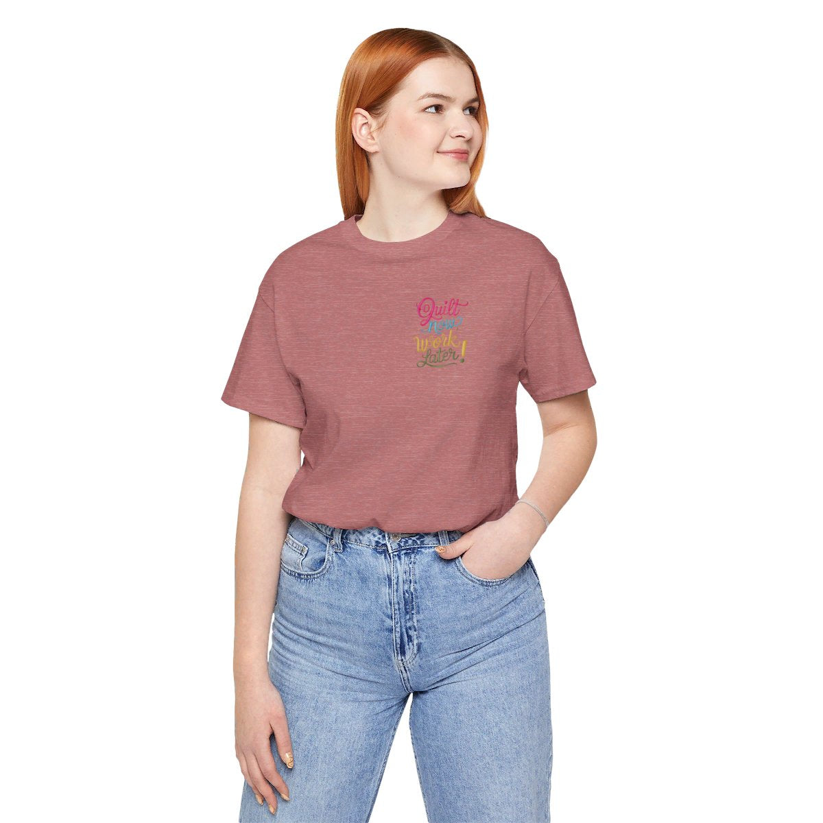 A Heather Mauve funny quilting T-shirt featuring bold, stylized text that reads "Quilt Now, Work Later" in various vibrant colors. The playful design captures the spirit of passionate quilters who prioritize their craft over other responsibilities.
