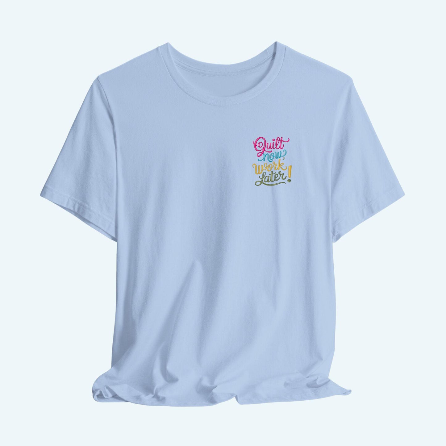 A funny quilting T-shirt featuring bold, stylized text that reads "Quilt Now, Work Later" in various vibrant colors. The playful design captures the spirit of passionate quilters who prioritize their craft over other responsibilities.