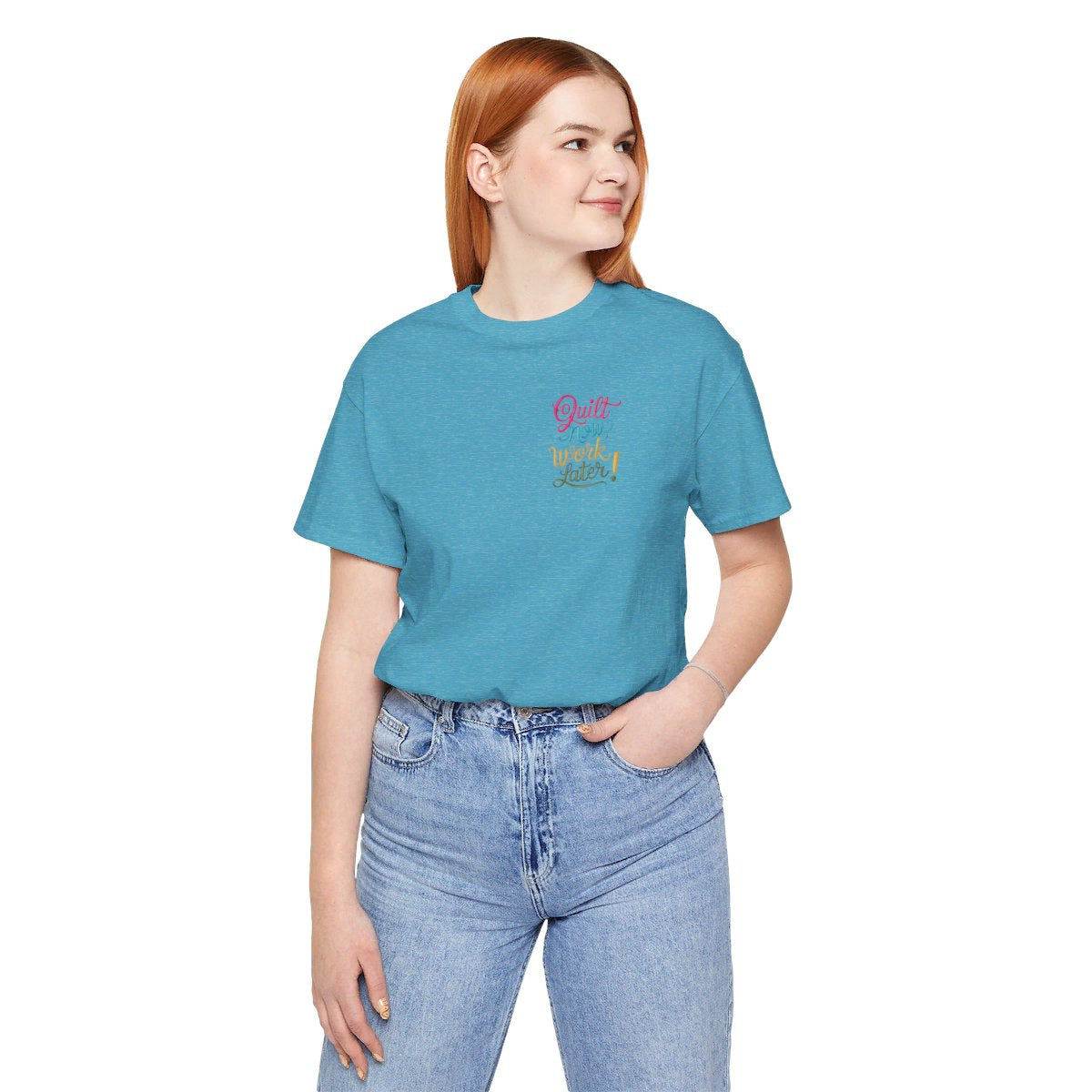 A Heather Aqua funny quilting T-shirt featuring bold, stylized text that reads "Quilt Now, Work Later" in various vibrant colors. The playful design captures the spirit of passionate quilters who prioritize their craft over other responsibilities.