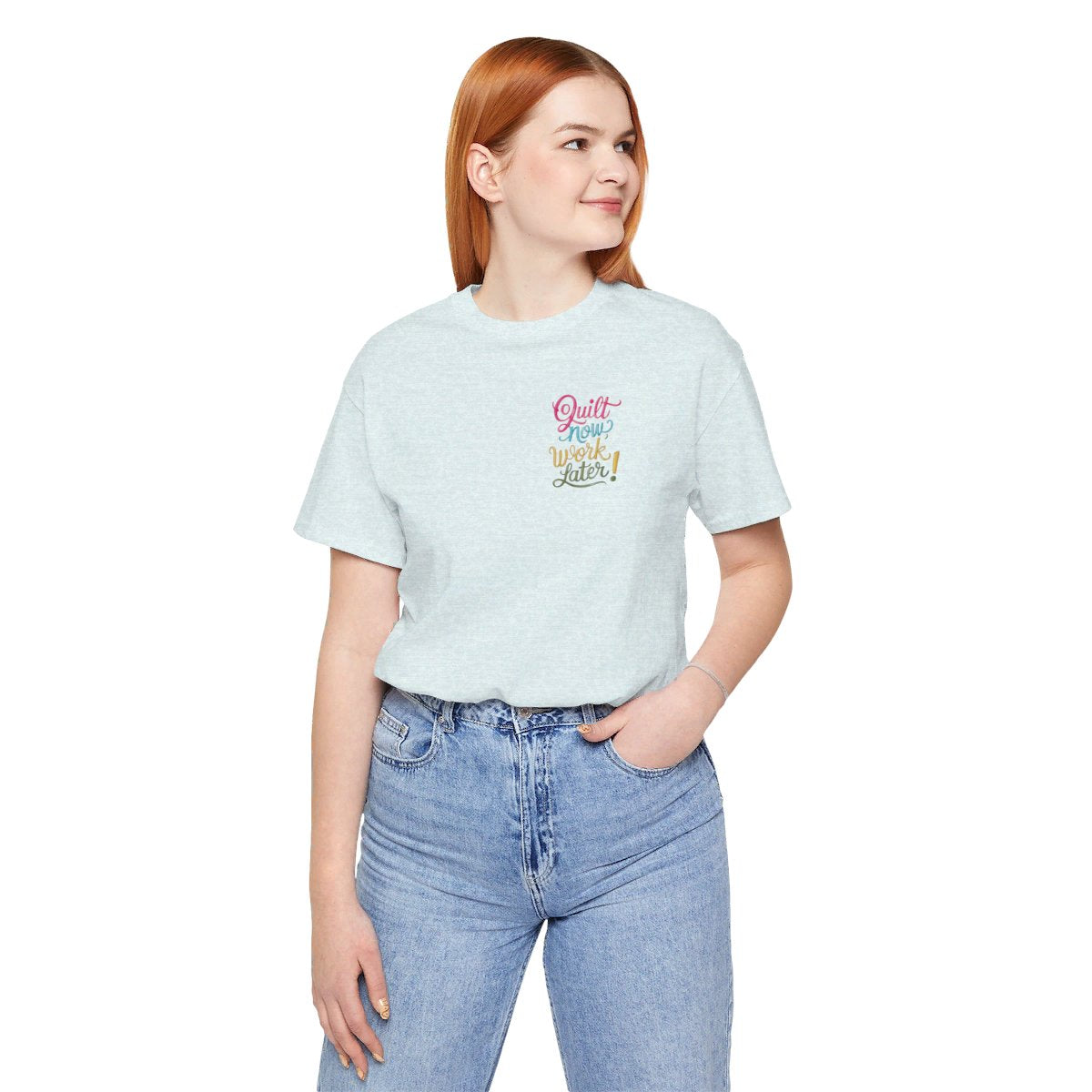 A Heather Ice Blue funny quilting T-shirt featuring bold, stylized text that reads "Quilt Now, Work Later" in various vibrant colors. The playful design captures the spirit of passionate quilters who prioritize their craft over other responsibilities.