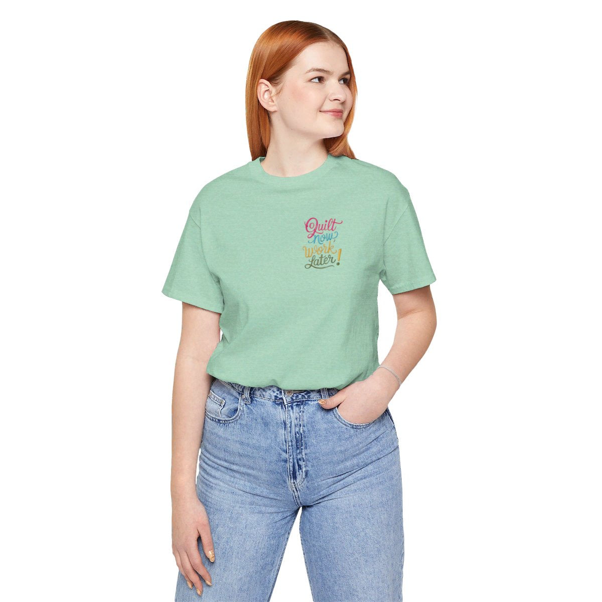 A Heather Mint funny quilting T-shirt featuring bold, stylized text that reads "Quilt Now, Work Later" in various vibrant colors. The playful design captures the spirit of passionate quilters who prioritize their craft over other responsibilities.
