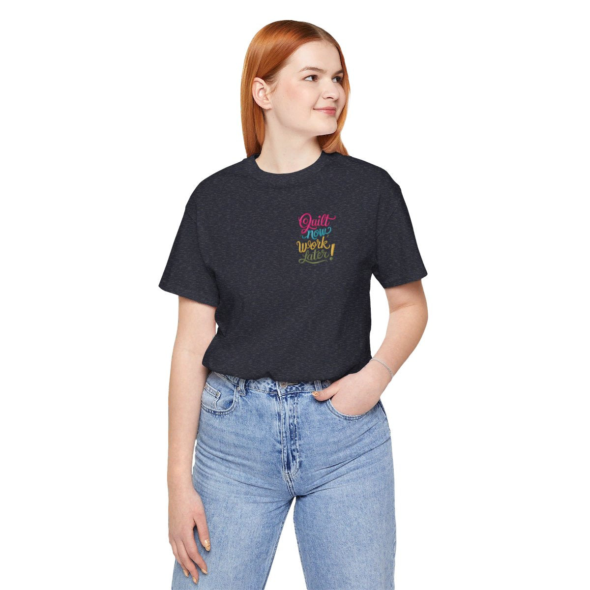 A Heather Navy funny quilting T-shirt featuring bold, stylized text that reads "Quilt Now, Work Later" in various vibrant colors. The playful design captures the spirit of passionate quilters who prioritize their craft over other responsibilities.