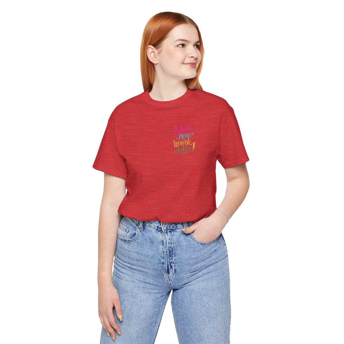 A Heather Red funny quilting T-shirt featuring bold, stylized text that reads "Quilt Now, Work Later" in various vibrant colors. The playful design captures the spirit of passionate quilters who prioritize their craft over other responsibilities.