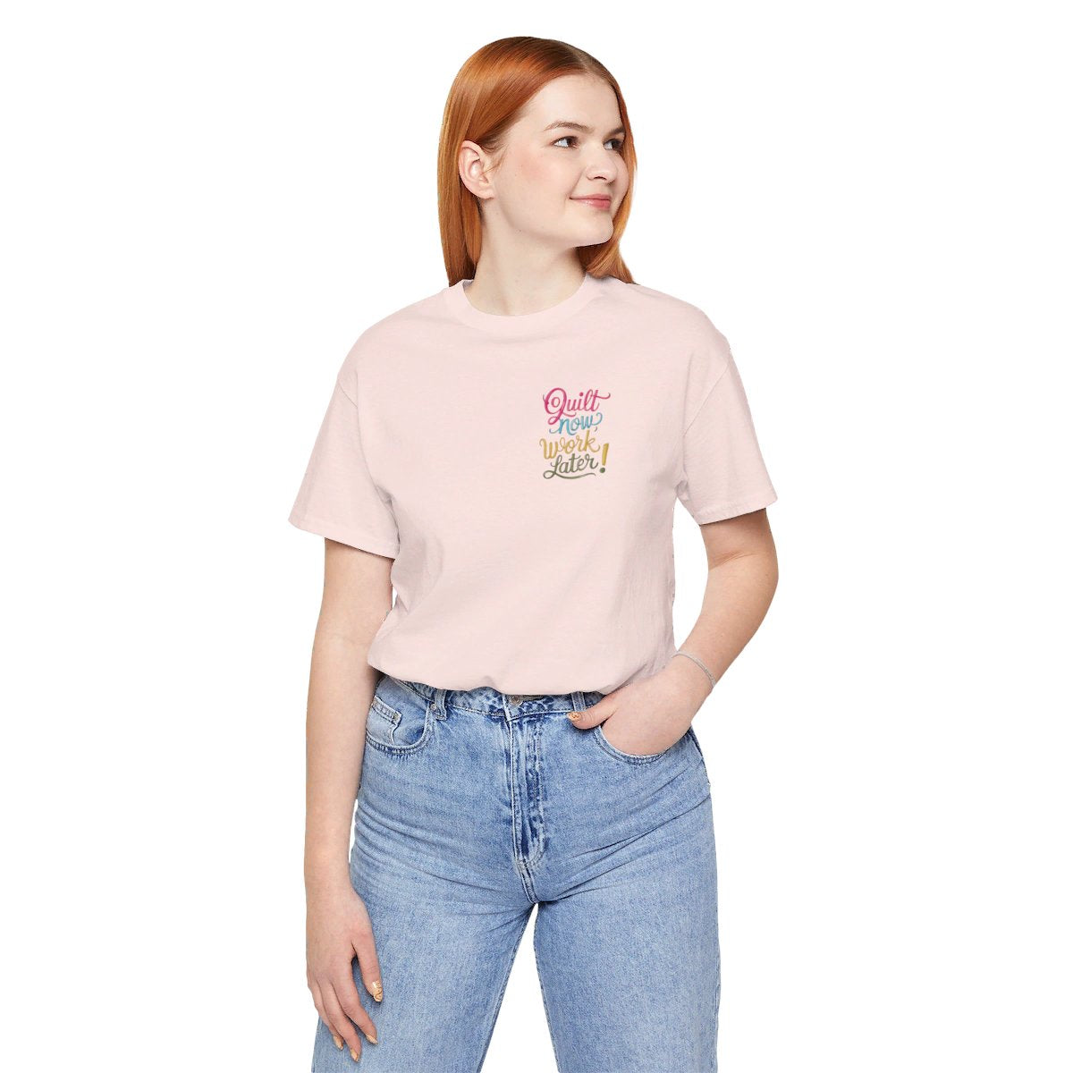 A Soft Pink funny quilting T-shirt featuring bold, stylized text that reads "Quilt Now, Work Later" in various vibrant colors. The playful design captures the spirit of passionate quilters who prioritize their craft over other responsibilities.
