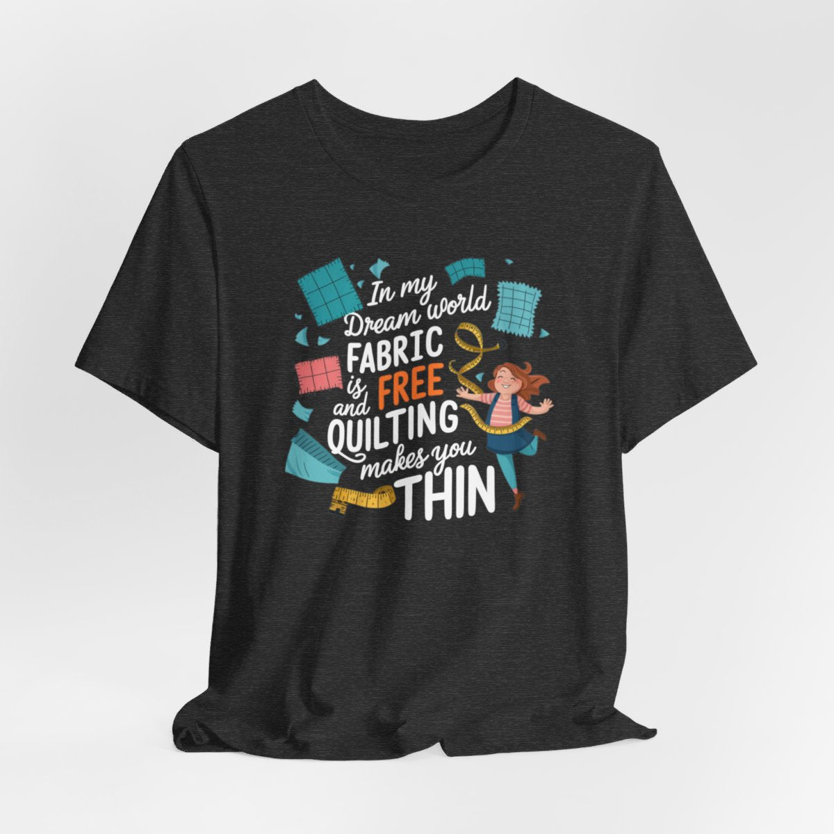 A Dark Grey Heather funny quilting T-Shirt with the phrase Fabric is Free and Quilting Makes You Thin in a fun font with a cheerful quilter jumping for joy