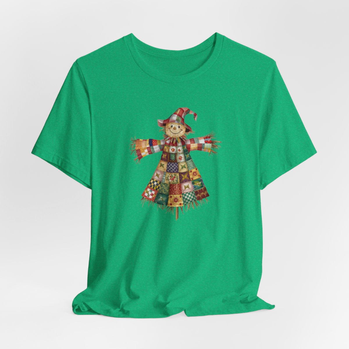 A Heather Kelly thanksgiving  quilting t-shirt featuring a smiling scarecrow made entirely of colorful quilt patterns. Wearing a patchwork hat and clothes with various quilt designs. Straw details on hands and neck. Cheerful autumn-themed illustration celebrating quilting craft.