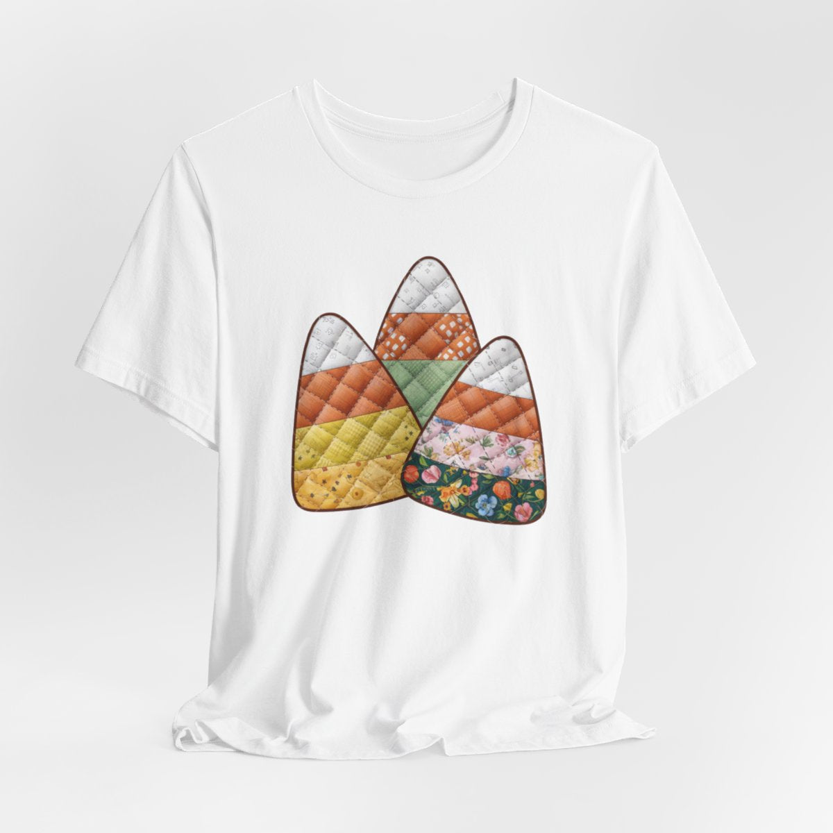 A White Halloween Quilting T-Shirt featuring three large candy corn shapes made of quilted fabrics with various patterns. Each candy corn section features different quilting motifs in autumn colors. Playful take on Halloween candy and quilting craft.