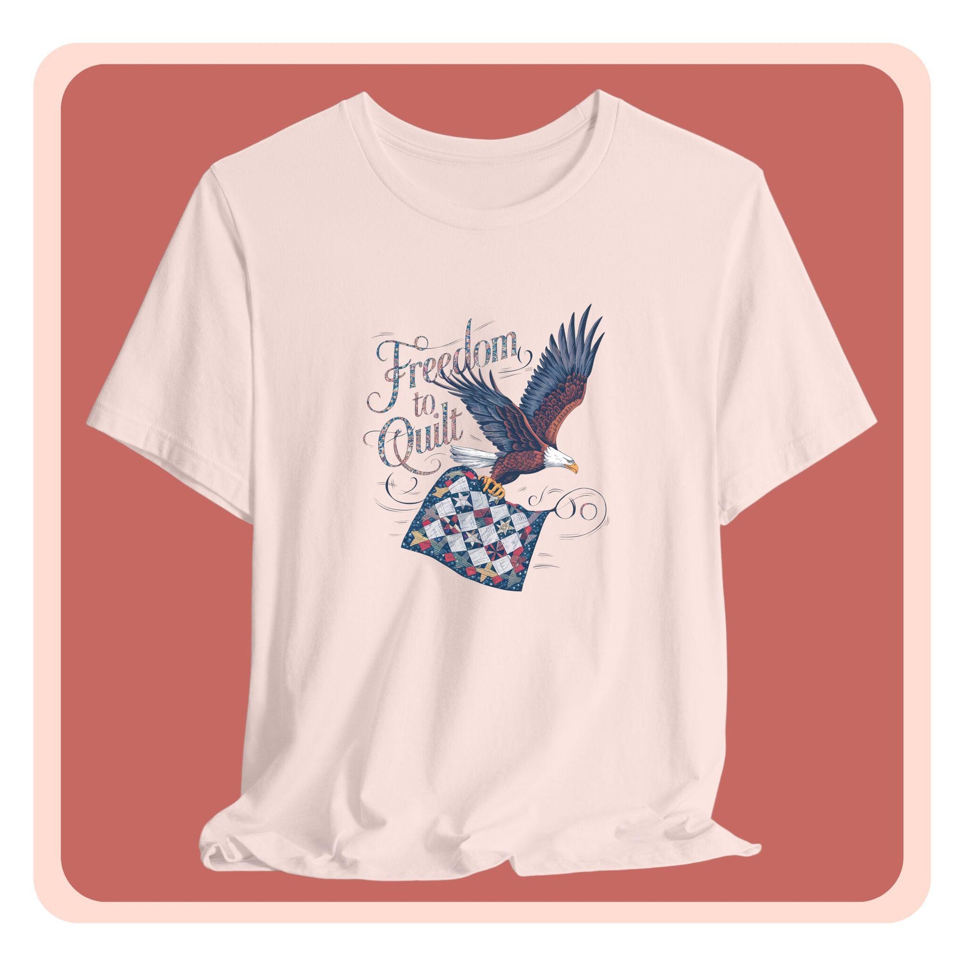 A T-shirt with detailed illustration of a bald eagle in flight, carrying a patchwork quilt. Text reads "Freedom to Quilt" in an ornate, patriotic font.