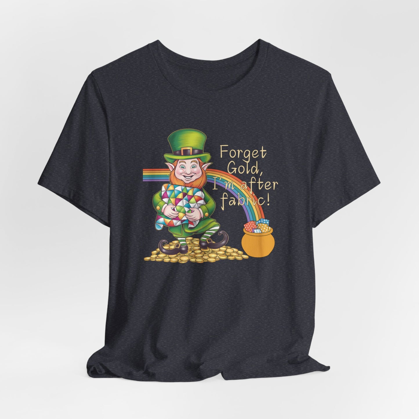 A Heather Navy short-sleeve t-shirt featuring a cheerful leprechaun holding a quilt, sitting on gold coins, with a rainbow leading to a fabric-filled pot and the phrase 'Forget Gold, I’m After Fabric!' Perfect for quilters celebrating St. Patrick’s Day.