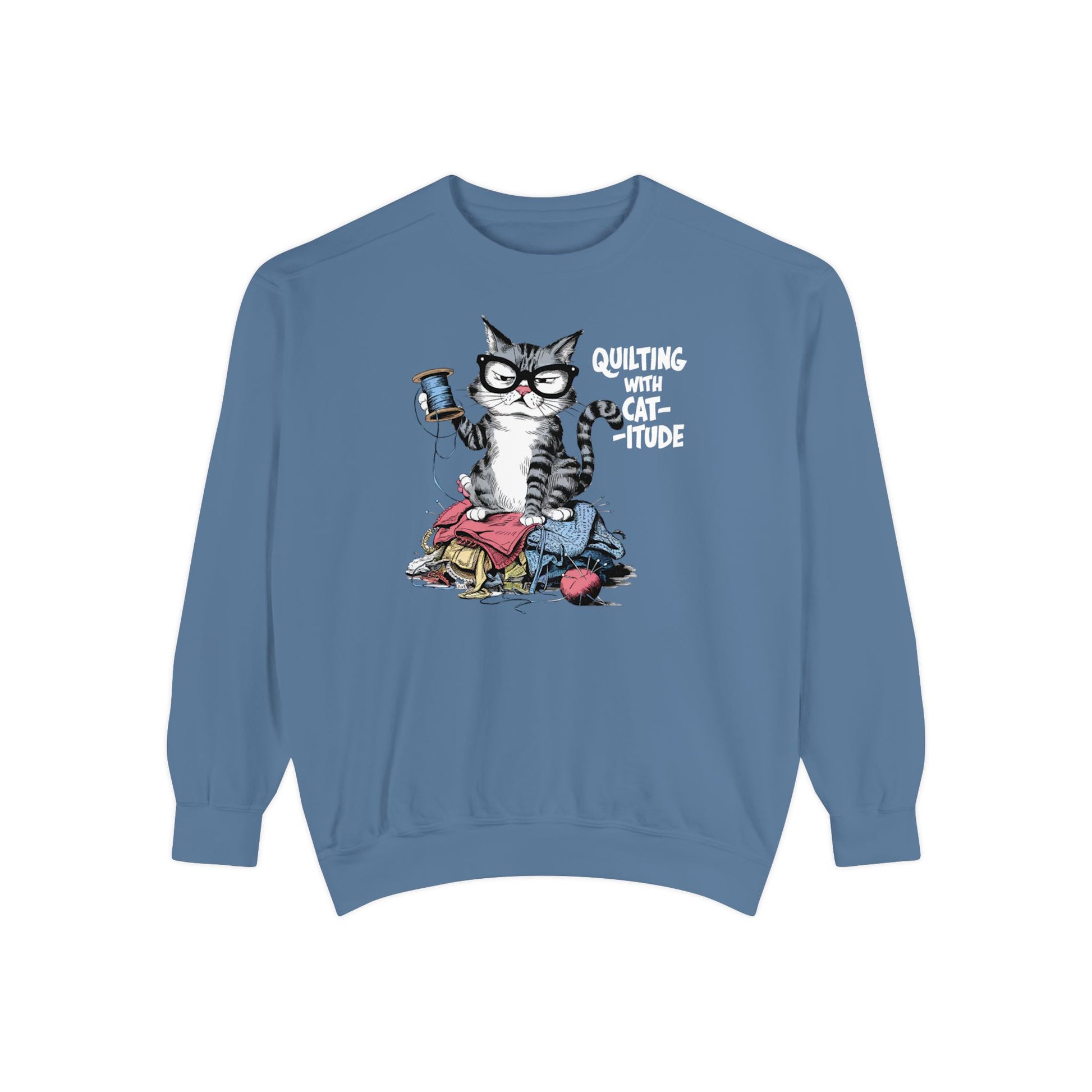 A Blue Jean sweatshirt featuring a sassy cartoon cat sitting on a pile of colorful fabric, holding a spool of thread, with the phrase 'Quilting with Cat-itude,' perfect for quilters and cat lovers.