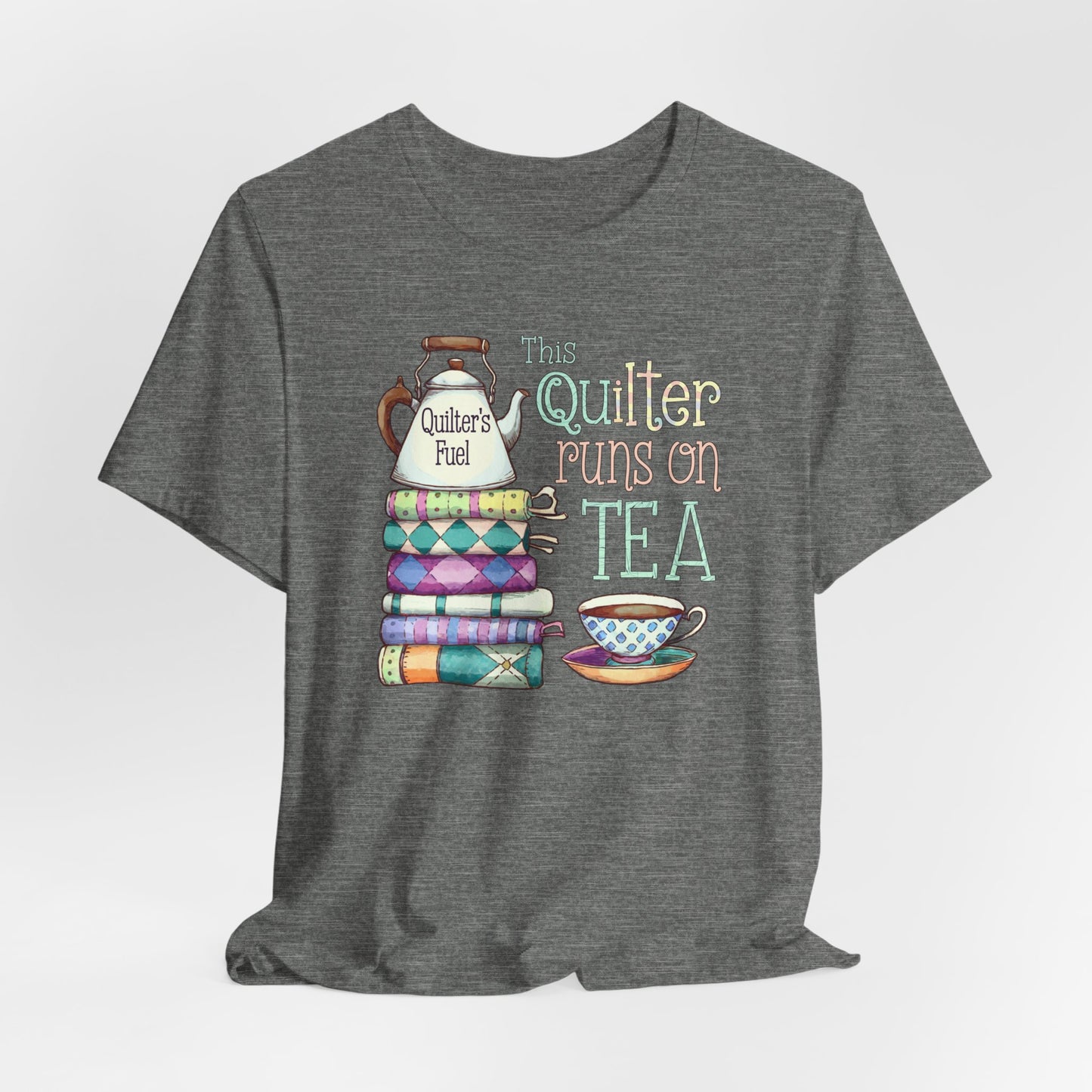 A Deep Heather t-shirt featuring a whimsical design of a stack of patchwork quilts with a teapot labeled 'Quilter's Fuel' and the phrase 'This Quilter Runs on Tea,' ideal for tea-loving quilters.