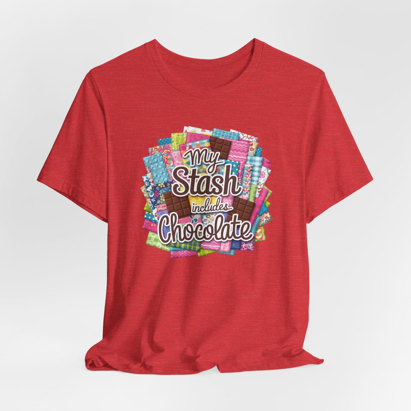 A Heather Red t-shirt featuring a colorful design of a fabric stash mixed with chocolate bars and the phrase 'My Stash Includes Chocolate,' perfect for quilters and chocolate lovers