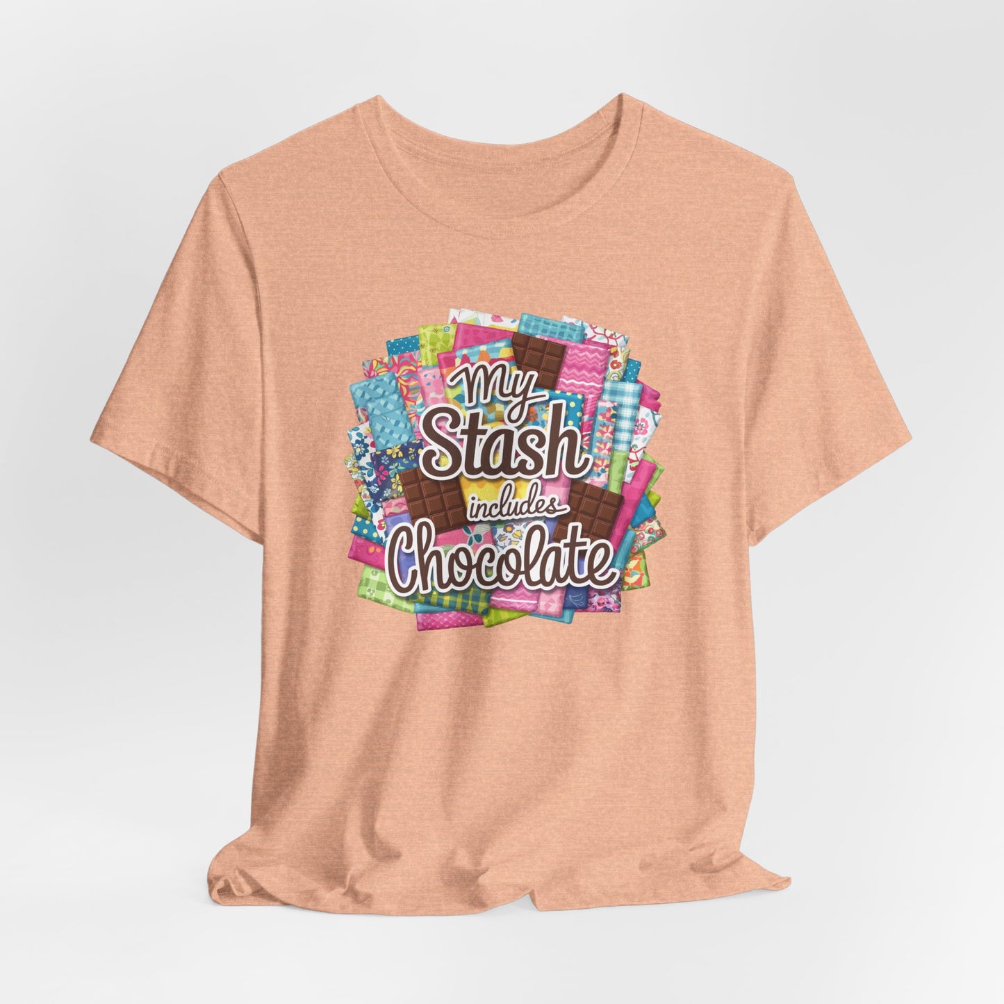 A Heather Peach t-shirt featuring a colorful design of a fabric stash mixed with chocolate bars and the phrase 'My Stash Includes Chocolate,' perfect for quilters and chocolate lovers