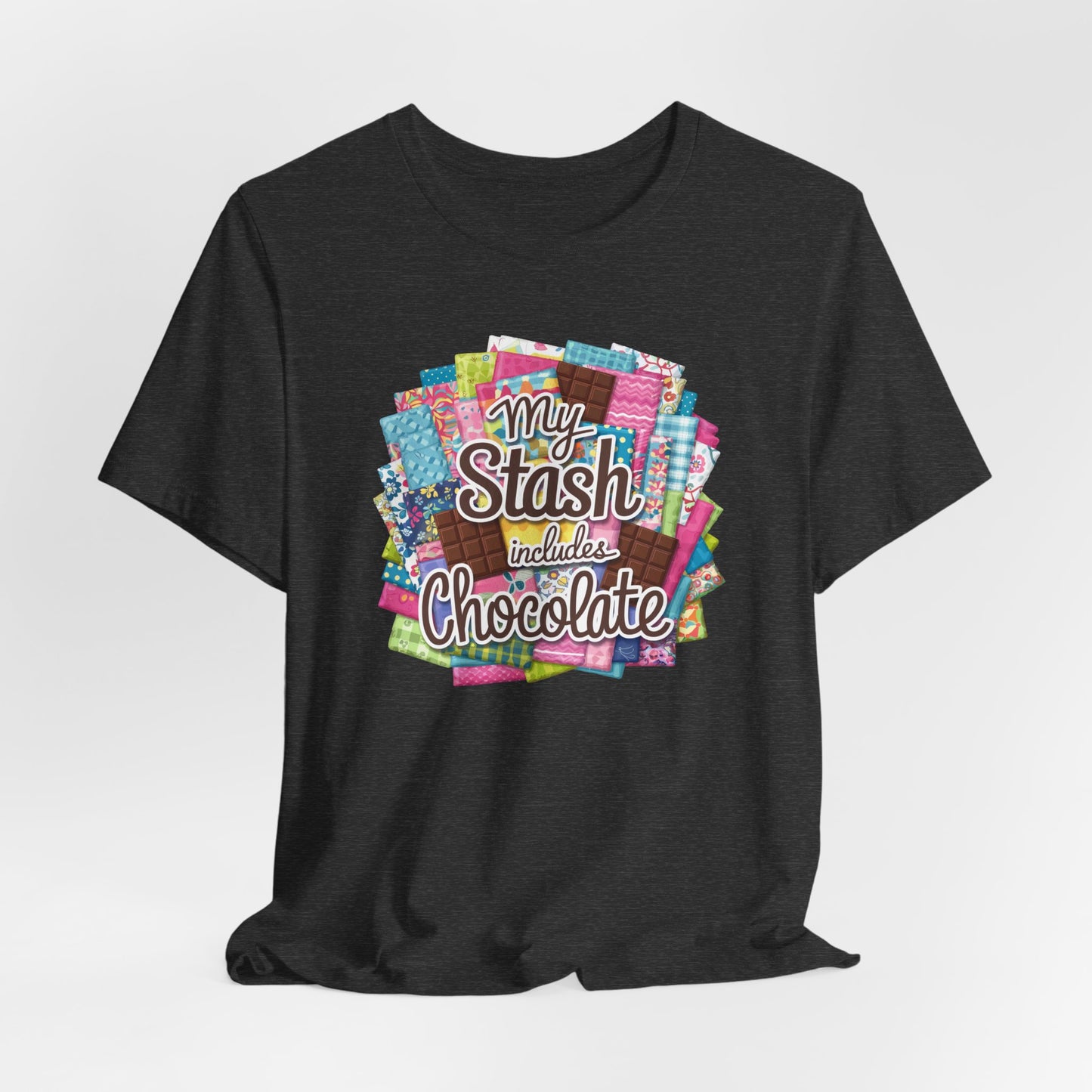 A Dark Grey Heather t-shirt featuring a colorful design of a fabric stash mixed with chocolate bars and the phrase 'My Stash Includes Chocolate,' perfect for quilters and chocolate lovers