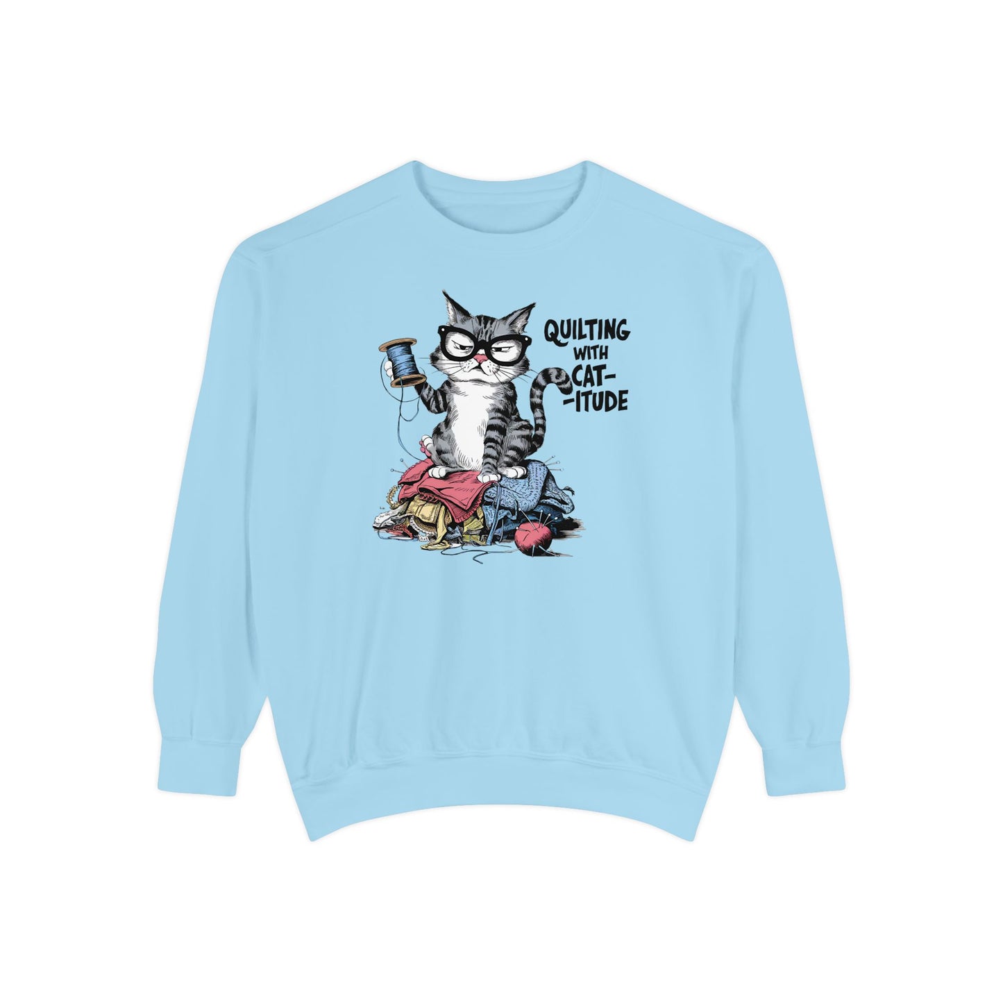 A Chambray sweatshirt featuring a sassy cartoon cat sitting on a pile of colorful fabric, holding a spool of thread, with the phrase 'Quilting with Cat-itude,' perfect for quilters and cat lovers.