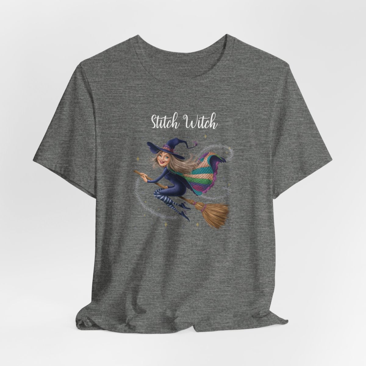 A Deep Heather Halloween Quilting T-Shirt featuring a witch riding broomstick on t-shirt design. Colorful patchwork quilt cape with various patterns. Sparkling magic and stars. Text reads "Stitch Witch". Ideal for quilters who enjoy magical themes.