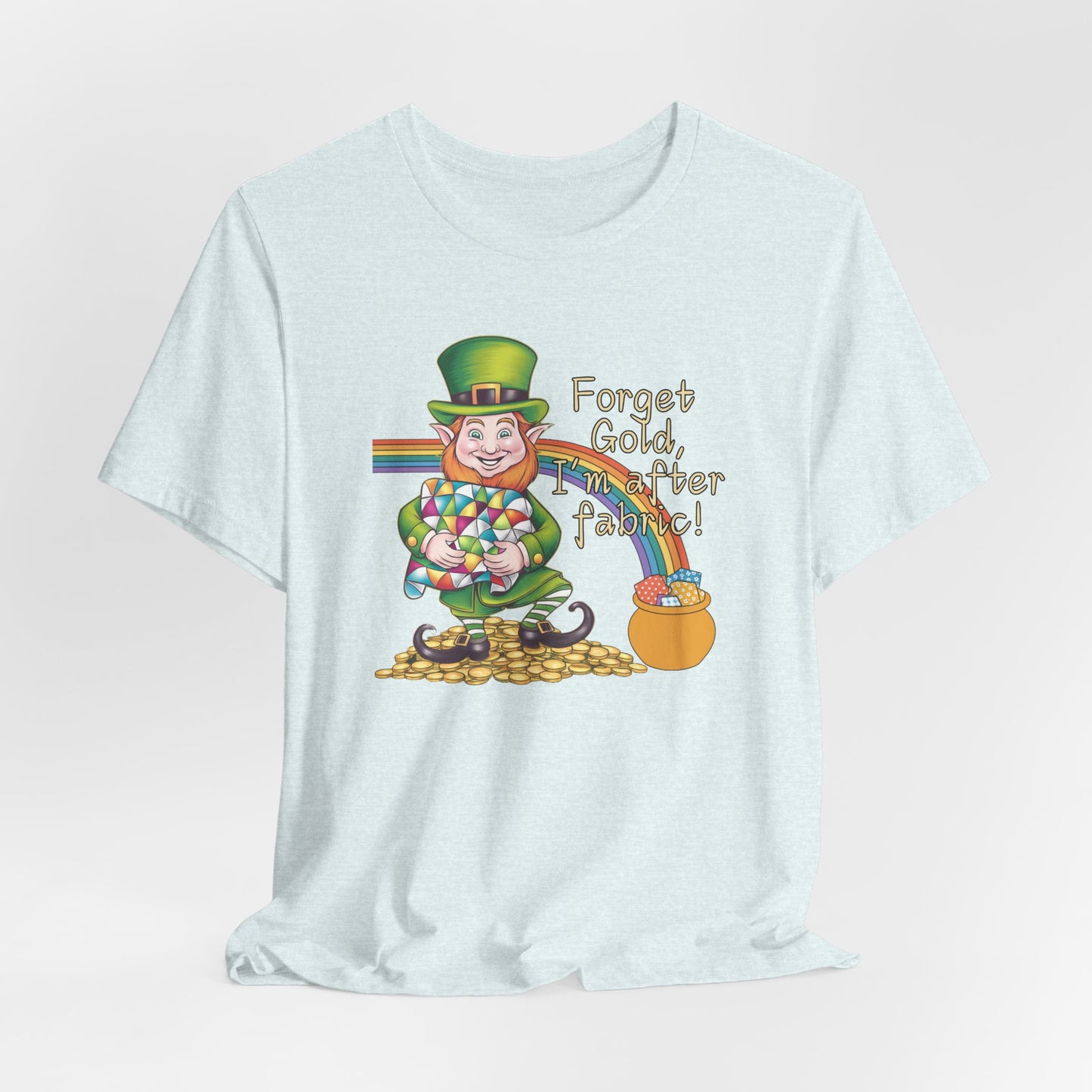 A Heather Ice Blue short-sleeve t-shirt featuring a cheerful leprechaun holding a quilt, sitting on gold coins, with a rainbow leading to a fabric-filled pot and the phrase 'Forget Gold, I’m After Fabric!' Perfect for quilters celebrating St. Patrick’s Day.