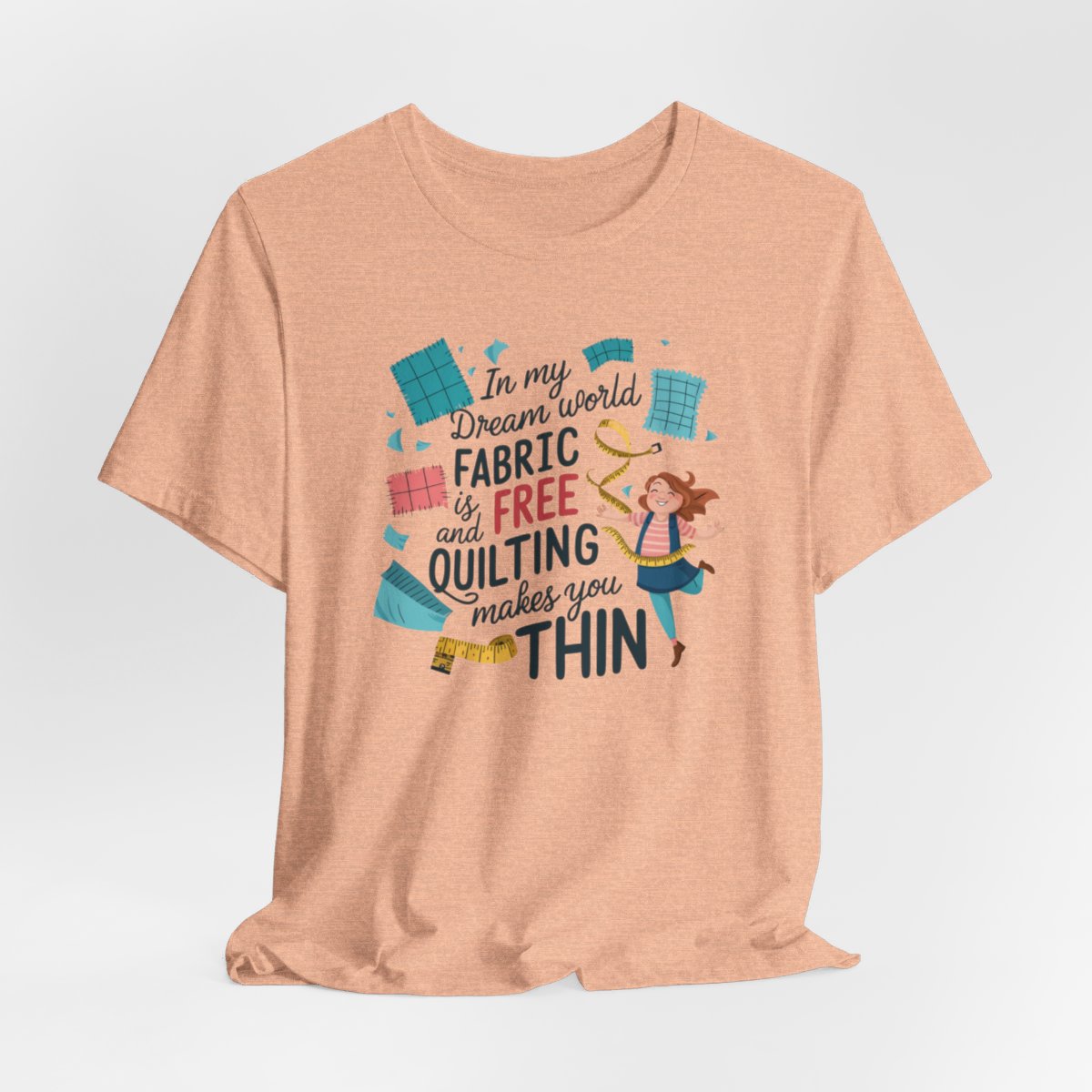 A Heather Peach funny quilting T-Shirt with the phrase Fabric is Free and Quilting Makes You Thin in a fun font with a cheerful quilter jumping for joy