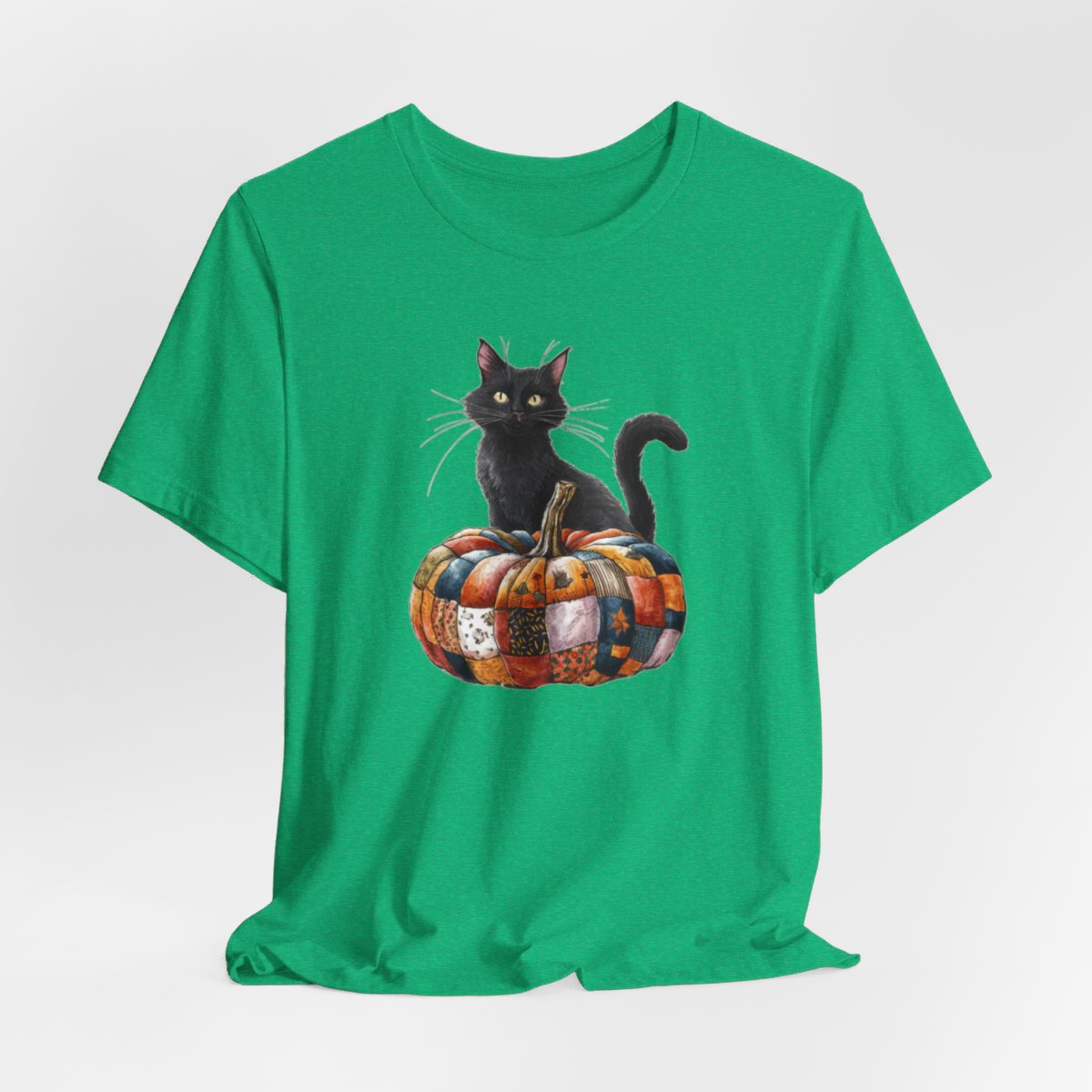 A Heather Kelly Halloween Quilting T-Shirt featuring a black cat sitting on colorful patchwork quilt pumpkin. Cat has yellow eyes and long whiskers. Pumpkin features various quilt patterns in autumn colors. Halloween-themed t-shirt design for quilting enthusiasts.