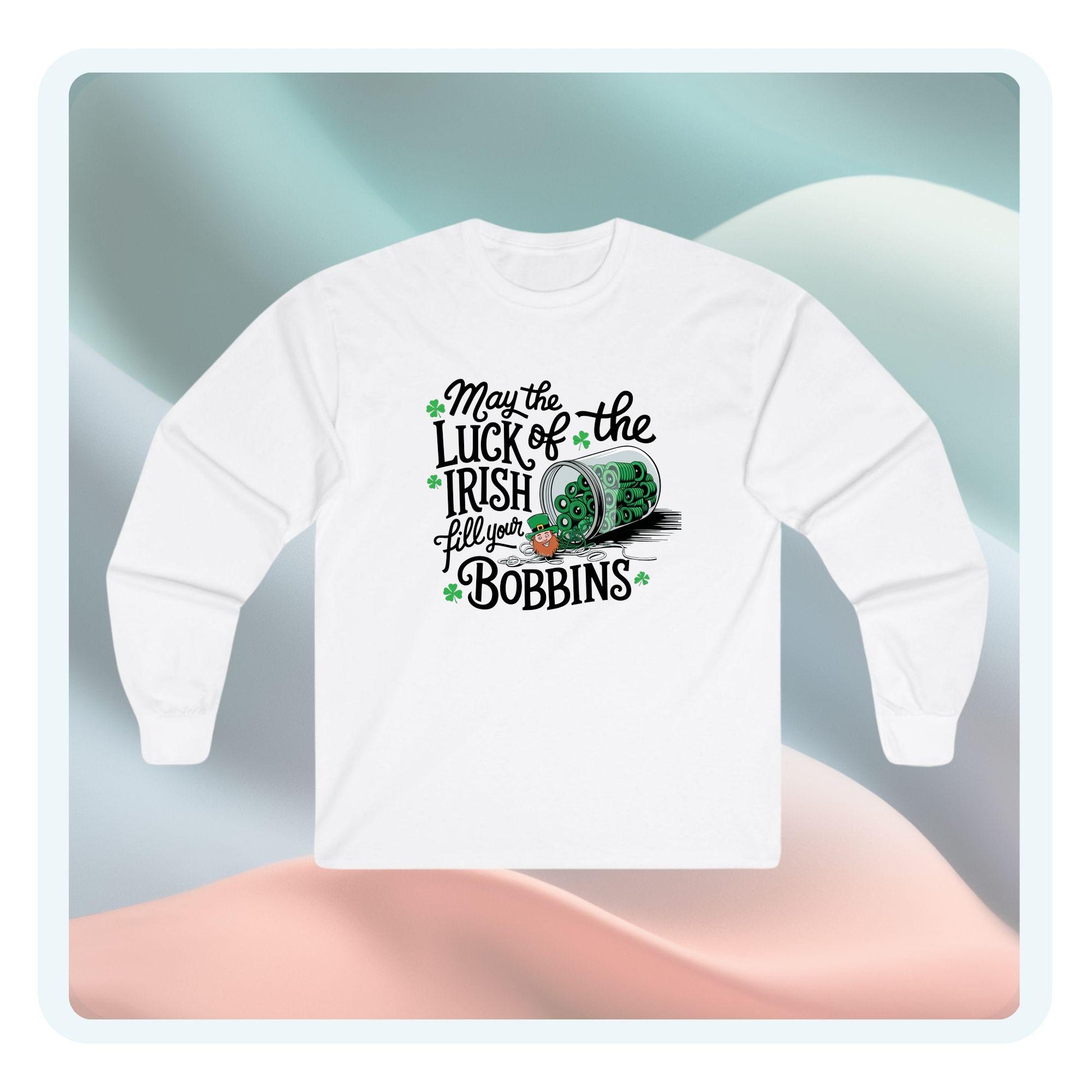 A long-sleeve t-shirt featuring a festive design with shamrocks, a spool of green thread, and the phrase 'May the Luck of the Irish Fill Your Bobbins,' perfect for quilters celebrating St. Patrick’s Day.