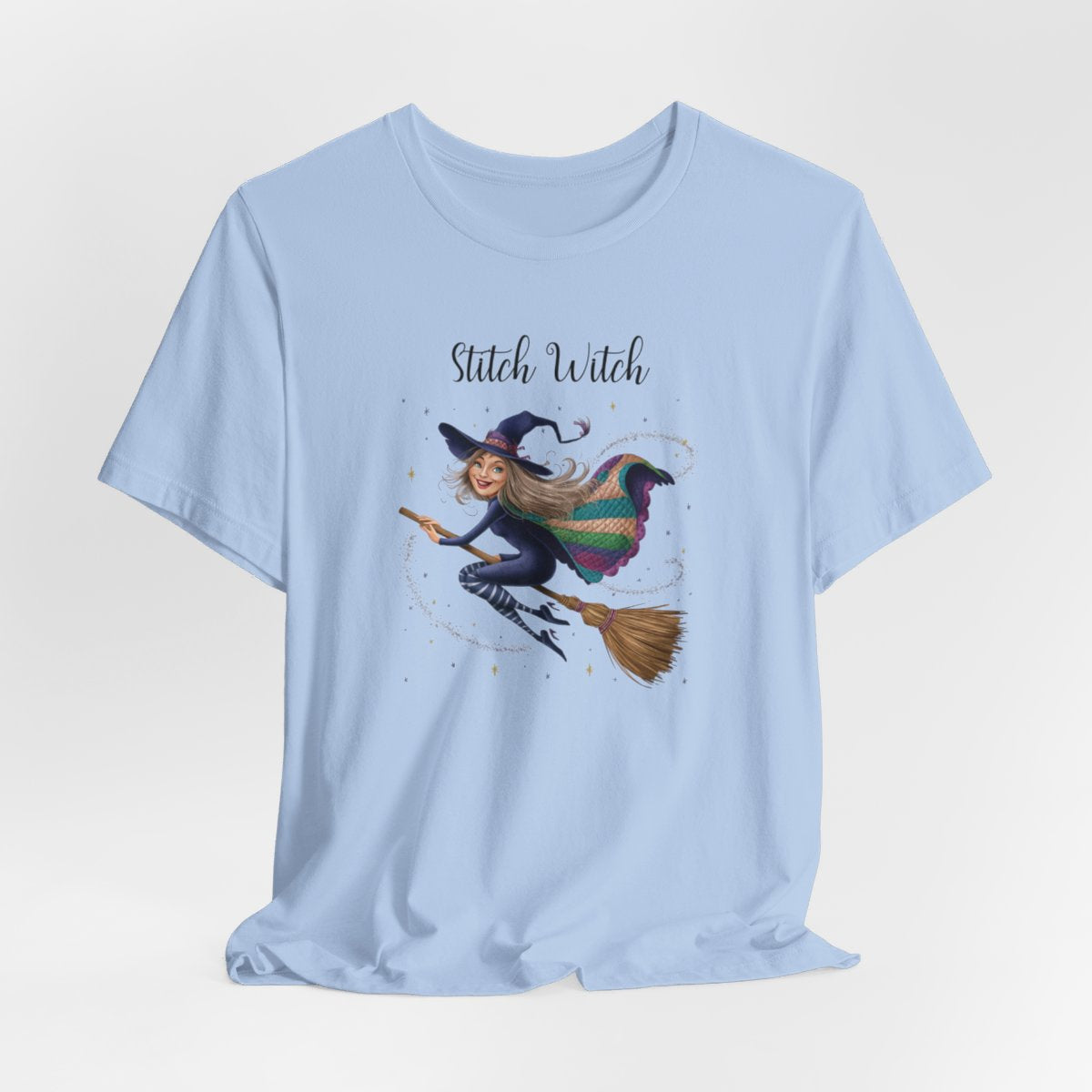 A Baby Blue Halloween Quilting T-Shirt featuring a witch riding broomstick on t-shirt design. Colorful patchwork quilt cape with various patterns. Sparkling magic and stars. Text reads "Stitch Witch". Ideal for quilters who enjoy magical themes.