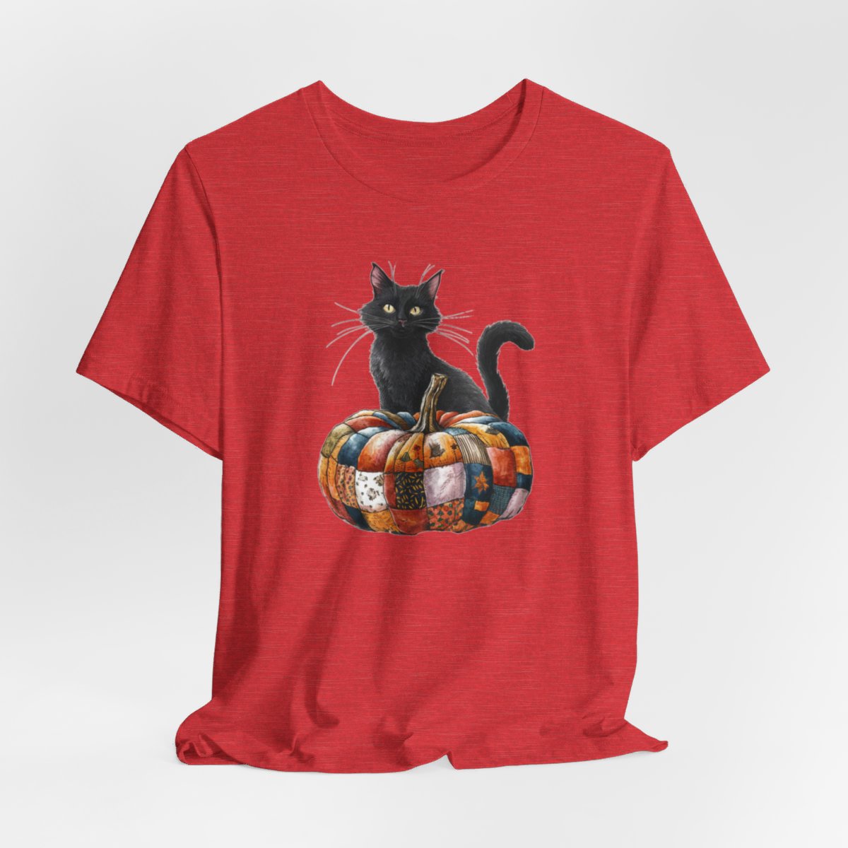 A Heather Red Halloween Quilting T-Shirt featuring a black cat sitting on colorful patchwork quilt pumpkin. Cat has yellow eyes and long whiskers. Pumpkin features various quilt patterns in autumn colors. Halloween-themed t-shirt design for quilting enthusiasts.