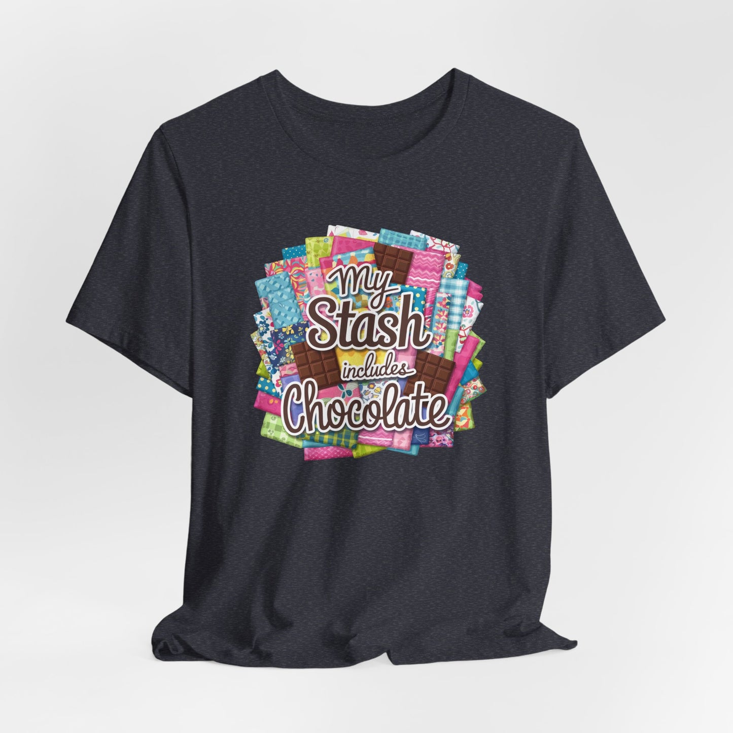 A Heather Navy t-shirt featuring a colorful design of a fabric stash mixed with chocolate bars and the phrase 'My Stash Includes Chocolate,' perfect for quilters and chocolate lovers