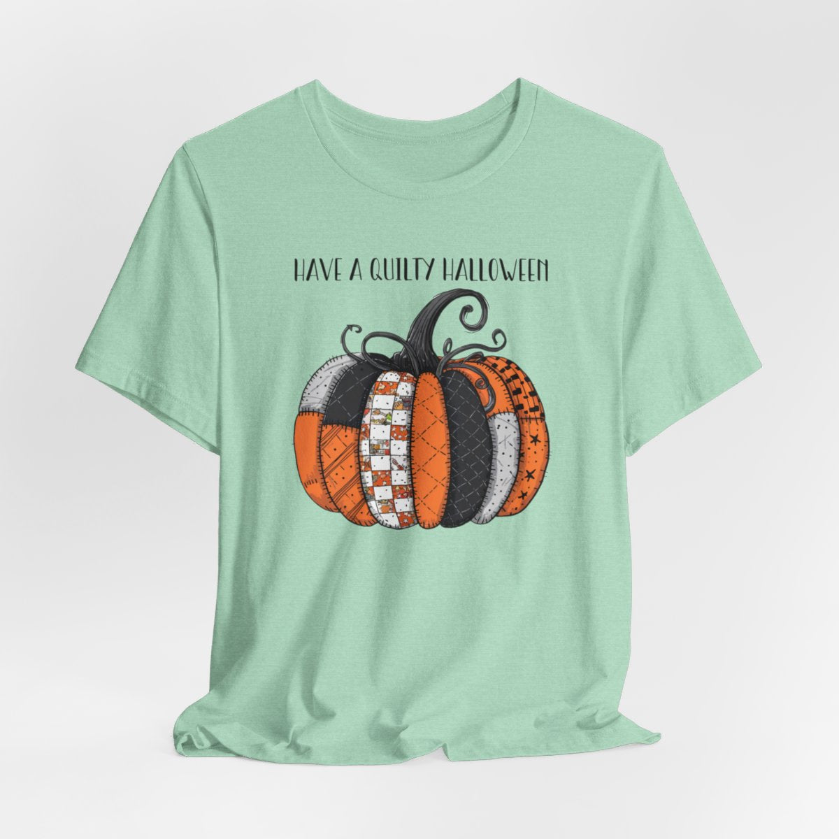 A Heather Mint Halloween Quilting T-Shirt featuring patchwork pumpkin with various quilt patterns. Mix of Halloween and traditional quilt motifs. Intricate stitching details. Text reads "Have a Quilty Halloween". Ideal for quilters who love Halloween.