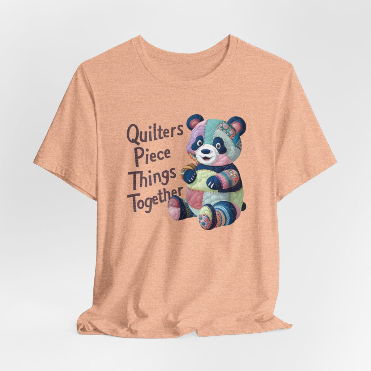 A Heather Peach fun T-Shirt with the phrase Quilters Piece Things Together with a patchwork panda design . The panda is made of colorful fabric scraps stitched together, creating a whimsical and crafty appearance. Perfect for quilting enthusiasts with a sense of humor.