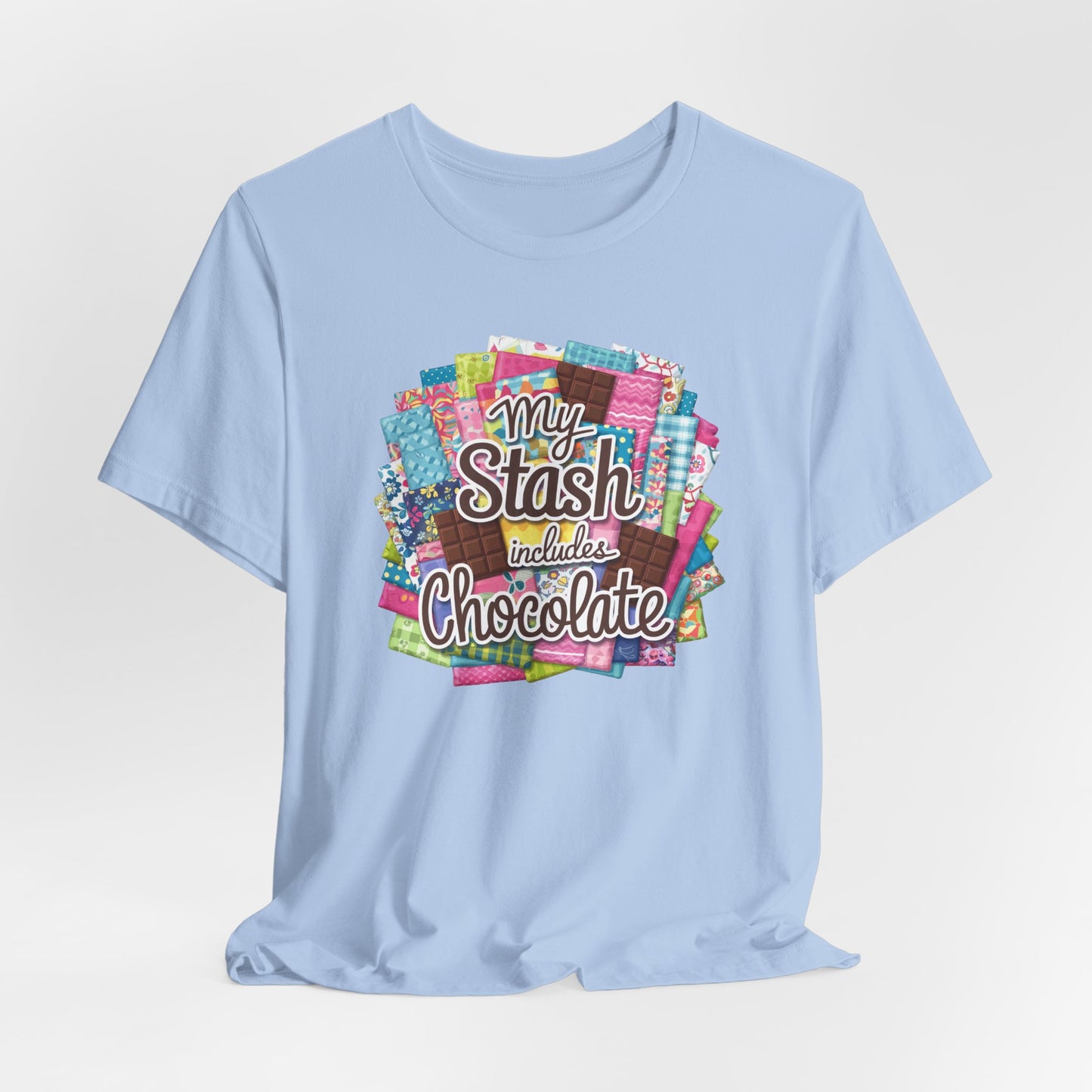 A Baby Blue t-shirt featuring a colorful design of a fabric stash mixed with chocolate bars and the phrase 'My Stash Includes Chocolate,' perfect for quilters and chocolate lovers