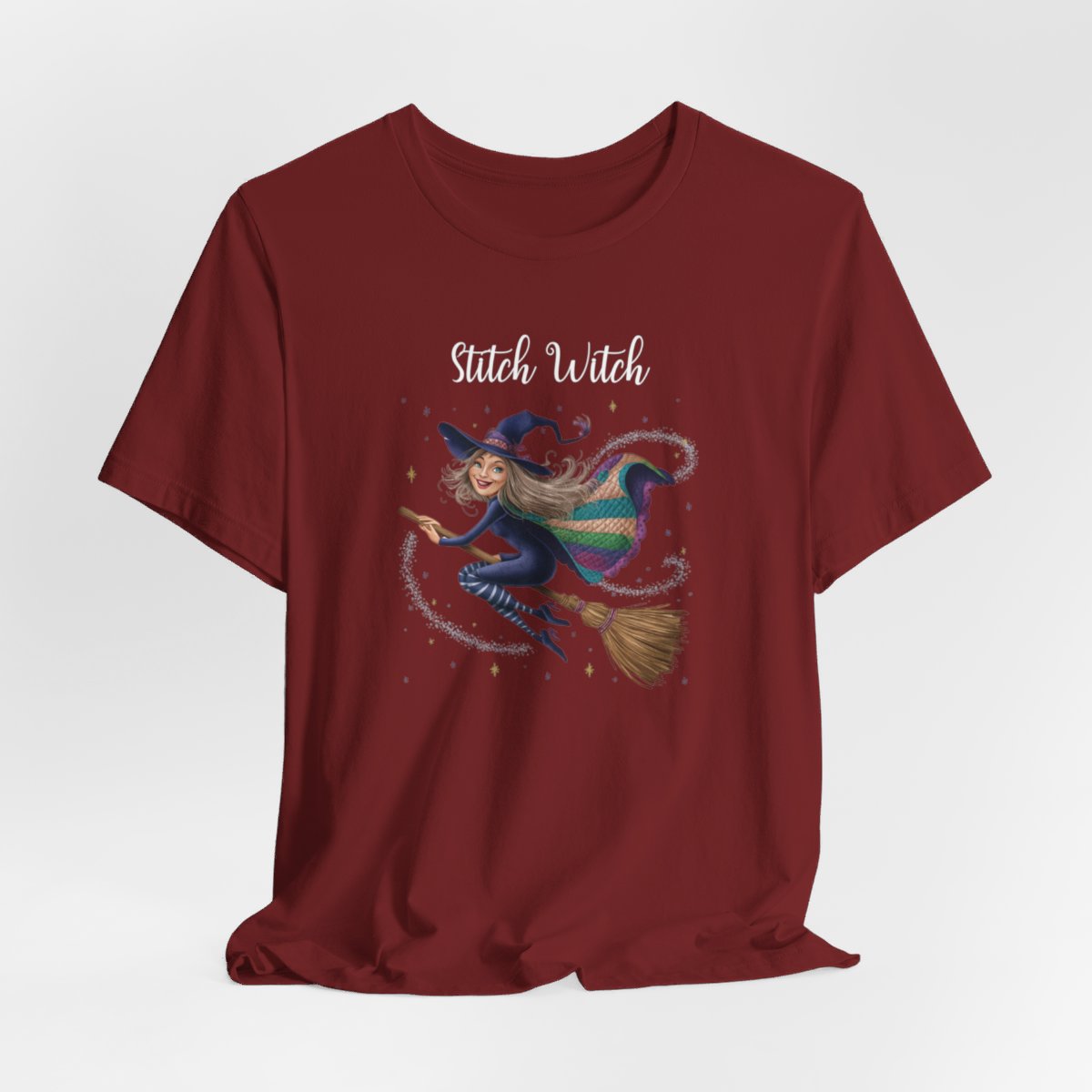 A Cardinal Halloween Quilting T-Shirt featuring a witch riding broomstick on t-shirt design. Colorful patchwork quilt cape with various patterns. Sparkling magic and stars. Text reads "Stitch Witch". Ideal for quilters who enjoy magical themes.