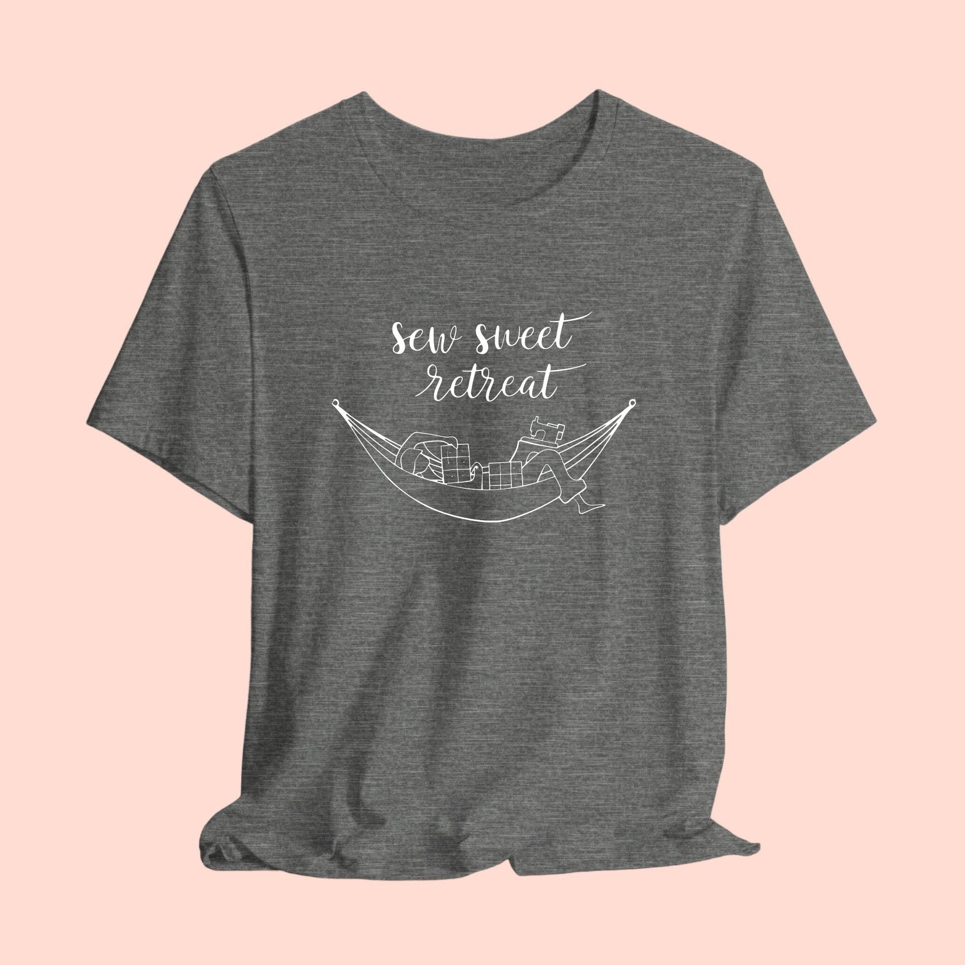 A T-Shirt with a black and white illustration of a hammock filled with quilting supplies like fabric squares and a sewing machine. Text above reads "Sew Sweet Retreat" in a flowing script font.