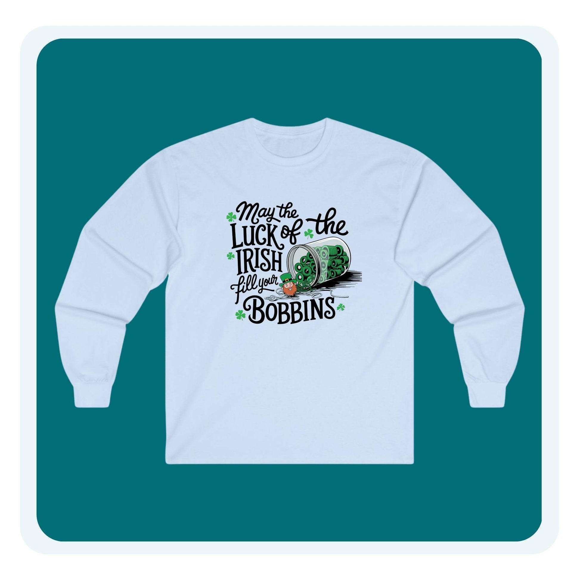 A long-sleeve t-shirt featuring a festive design with shamrocks, a spool of green thread, and the phrase 'May the Luck of the Irish Fill Your Bobbins,' perfect for quilters celebrating St. Patrick’s Day.