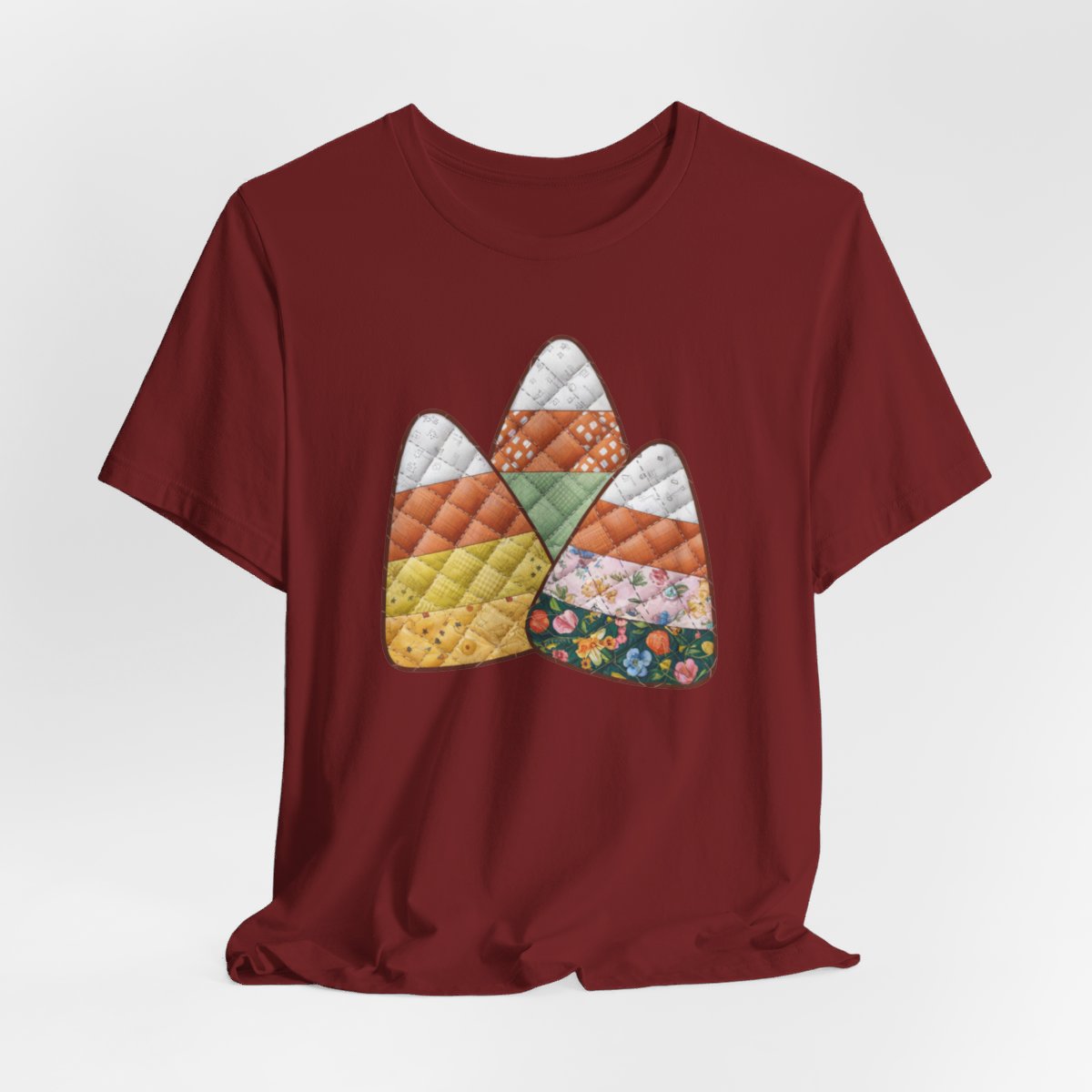 A Cardinal Halloween Quilting T-Shirt featuring three large candy corn shapes made of quilted fabrics with various patterns. Each candy corn section features different quilting motifs in autumn colors. Playful take on Halloween candy and quilting craft.