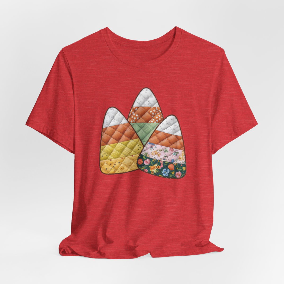 A Heather Red Halloween Quilting T-Shirt featuring three large candy corn shapes made of quilted fabrics with various patterns. Each candy corn section features different quilting motifs in autumn colors. Playful take on Halloween candy and quilting craft.