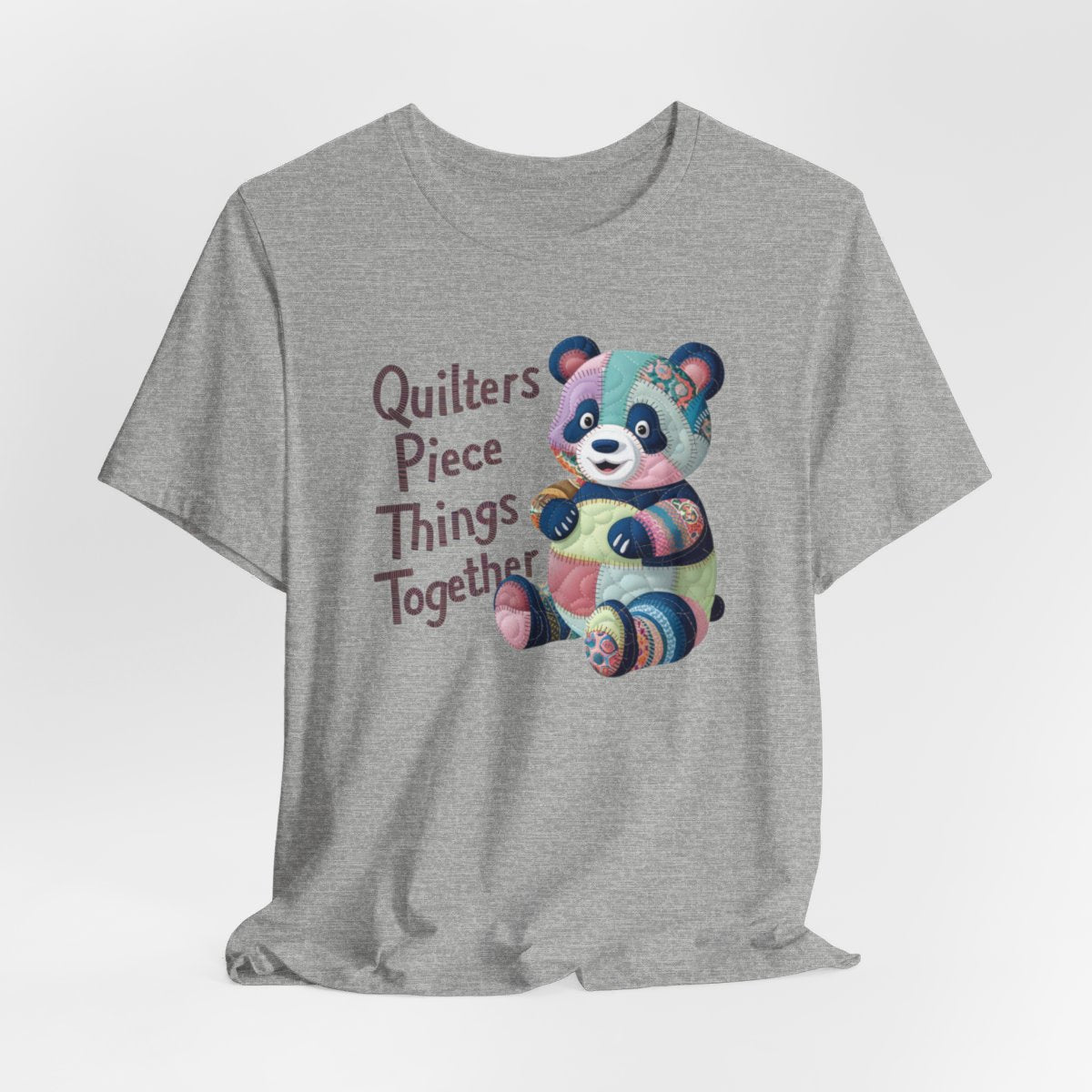 An Athletic Heather fun T-Shirt with the phrase Quilters Piece Things Together with a patchwork panda design . The panda is made of colorful fabric scraps stitched together, creating a whimsical and crafty appearance. Perfect for quilting enthusiasts with a sense of humor.