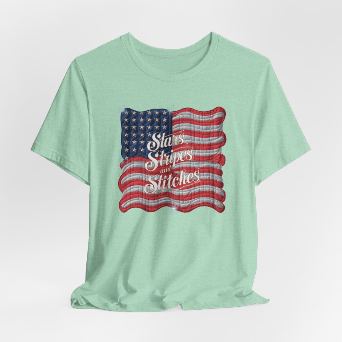 A Heather Mint T-shirt featuring quilted American flag design with text "Stars Stripes and Stitches" overlaid in stylized, patriotic font. Fireworks accent the corners.