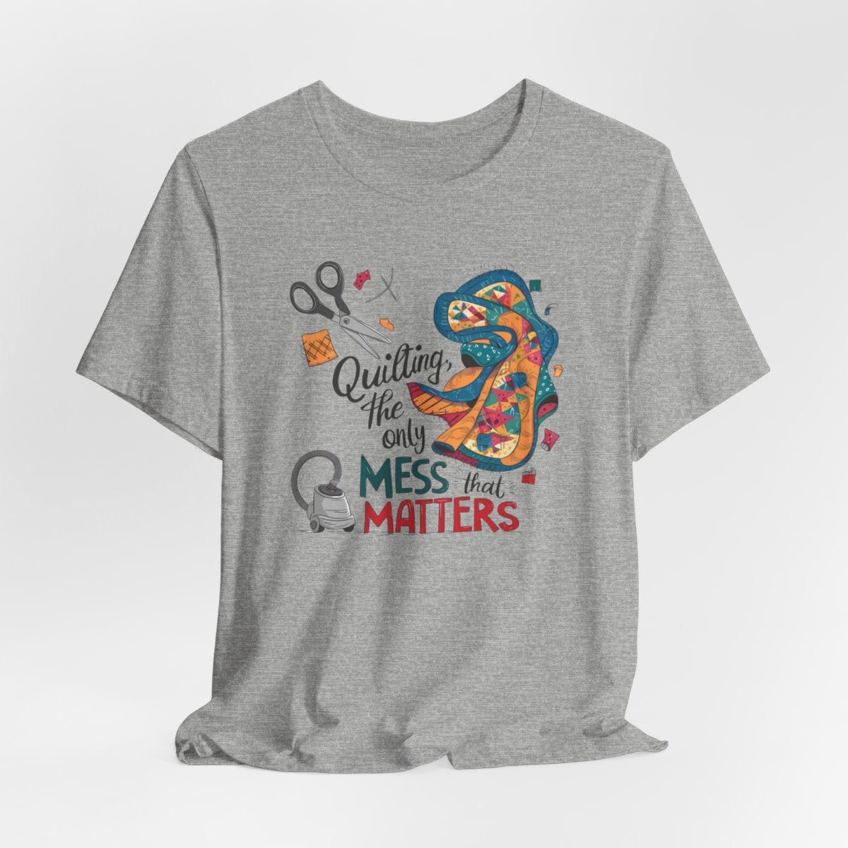 An Athletic Heather fun T-Shirt with the phrase Quilting, the Only Mess that Matters and illustrations of fabric scraps, scissors, and a vacuum cleaner. Colorful quilt patterns swirl around the text, creating a playful and relatable design for quilting enthusiasts.