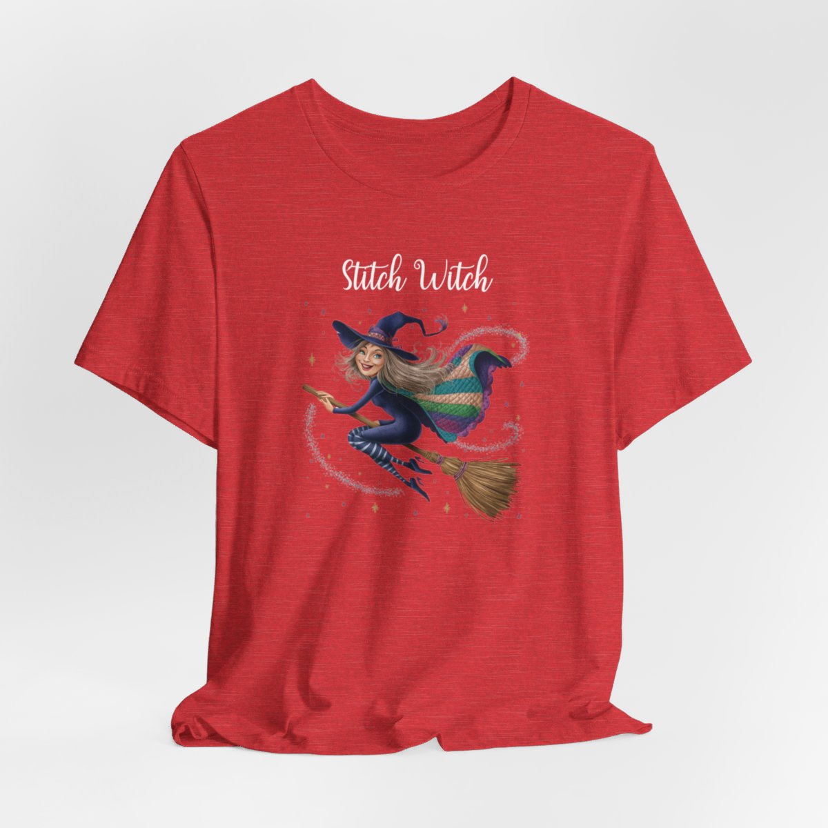 A Heather Red Halloween Quilting T-Shirt featuring a witch riding broomstick on t-shirt design. Colorful patchwork quilt cape with various patterns. Sparkling magic and stars. Text reads "Stitch Witch". Ideal for quilters who enjoy magical themes.