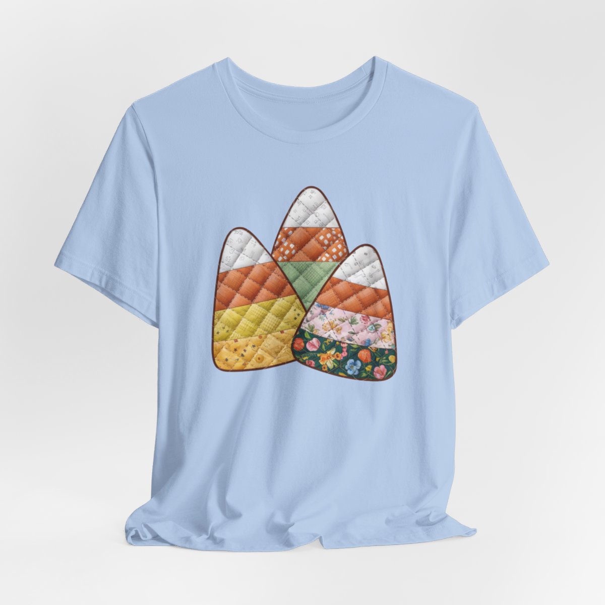 A Baby Blue Halloween Quilting T-Shirt featuring three large candy corn shapes made of quilted fabrics with various patterns. Each candy corn section features different quilting motifs in autumn colors. Playful take on Halloween candy and quilting craft.