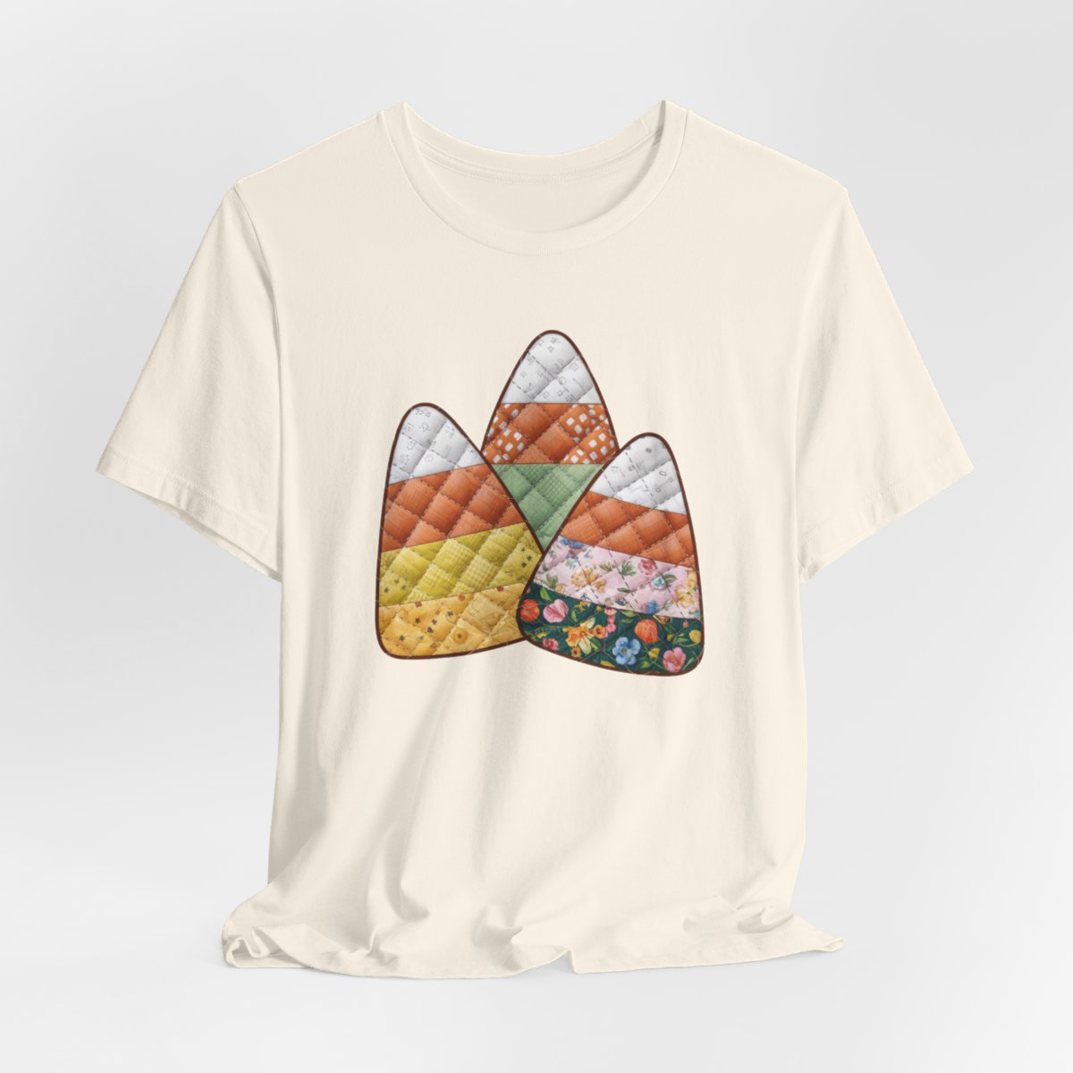 A Natural Halloween Quilting T-Shirt featuring three large candy corn shapes made of quilted fabrics with various patterns. Each candy corn section features different quilting motifs in autumn colors. Playful take on Halloween candy and quilting craft.