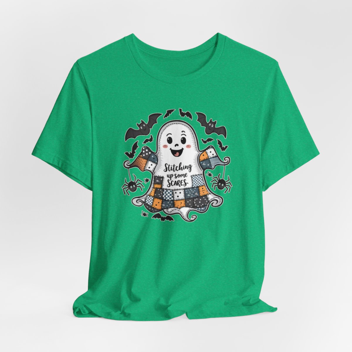 A Heather Kelly Halloween Quilting T-Shirt featuring a smiling ghost with quilted patchwork body. Halloween-themed quilt patterns. Cute bats and spiders around ghost. Text reads "Stitching up some Scares". Ideal for quilters who enjoy Halloween themes.