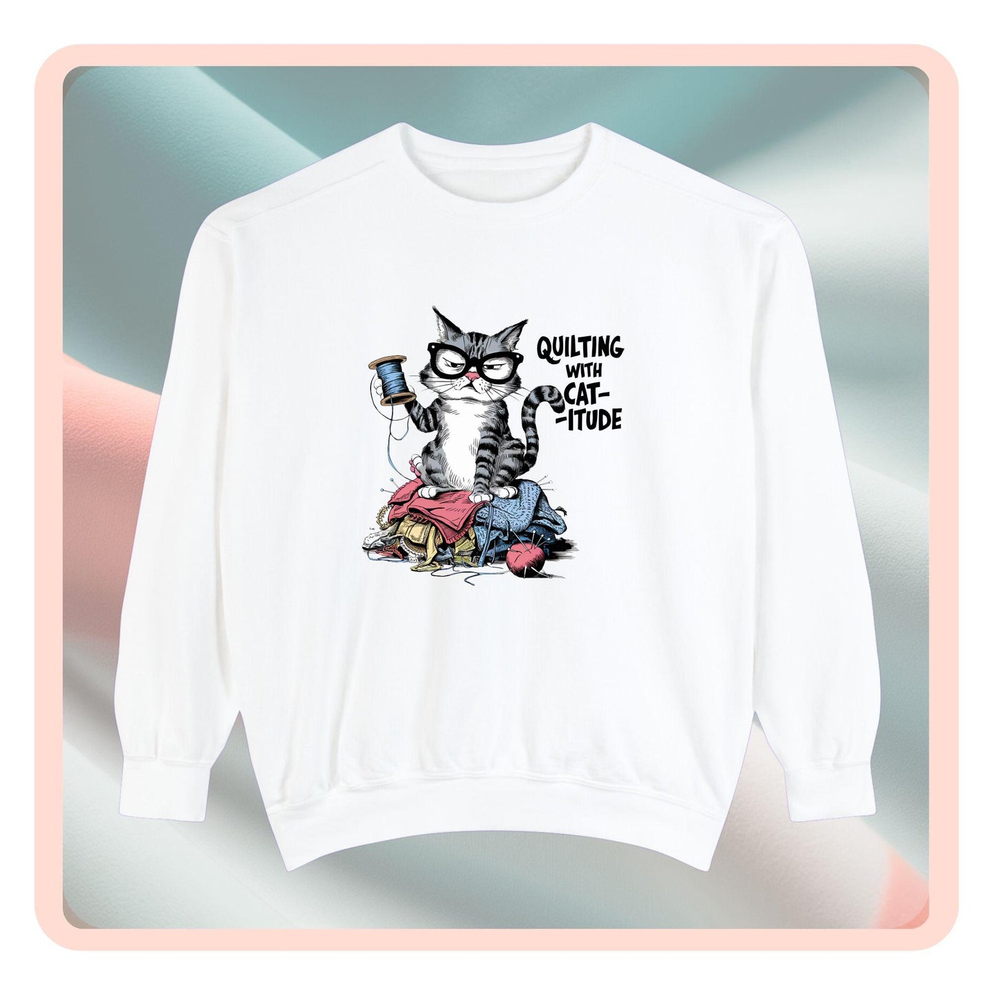 A sweatshirt featuring a sassy cartoon cat sitting on a pile of colorful fabric, holding a spool of thread, with the phrase 'Quilting with Cat-itude,' perfect for quilters and cat lovers.