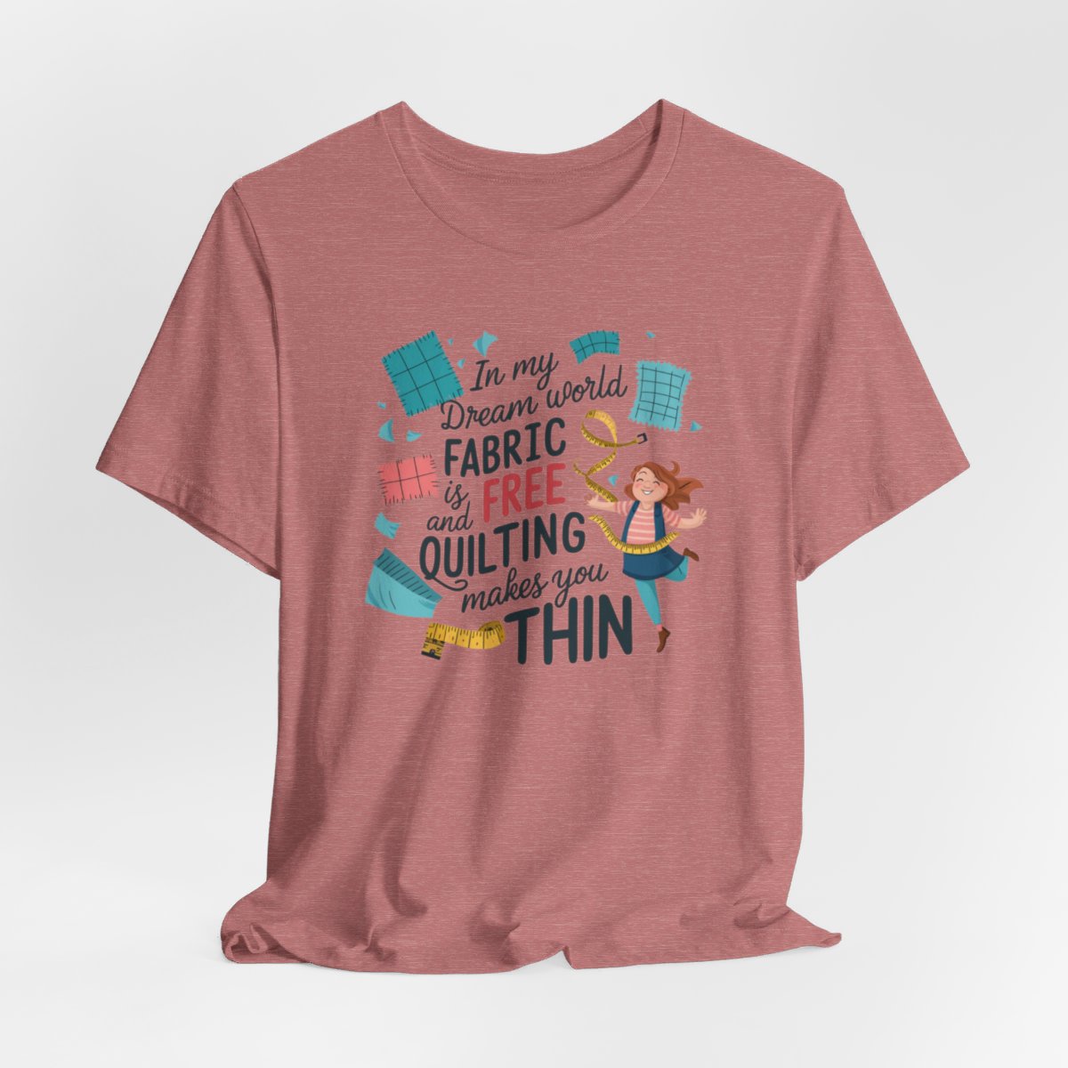 A Heather Mauve funny quilting T-Shirt with the phrase Fabric is Free and Quilting Makes You Thin in a fun font with a cheerful quilter jumping for joy