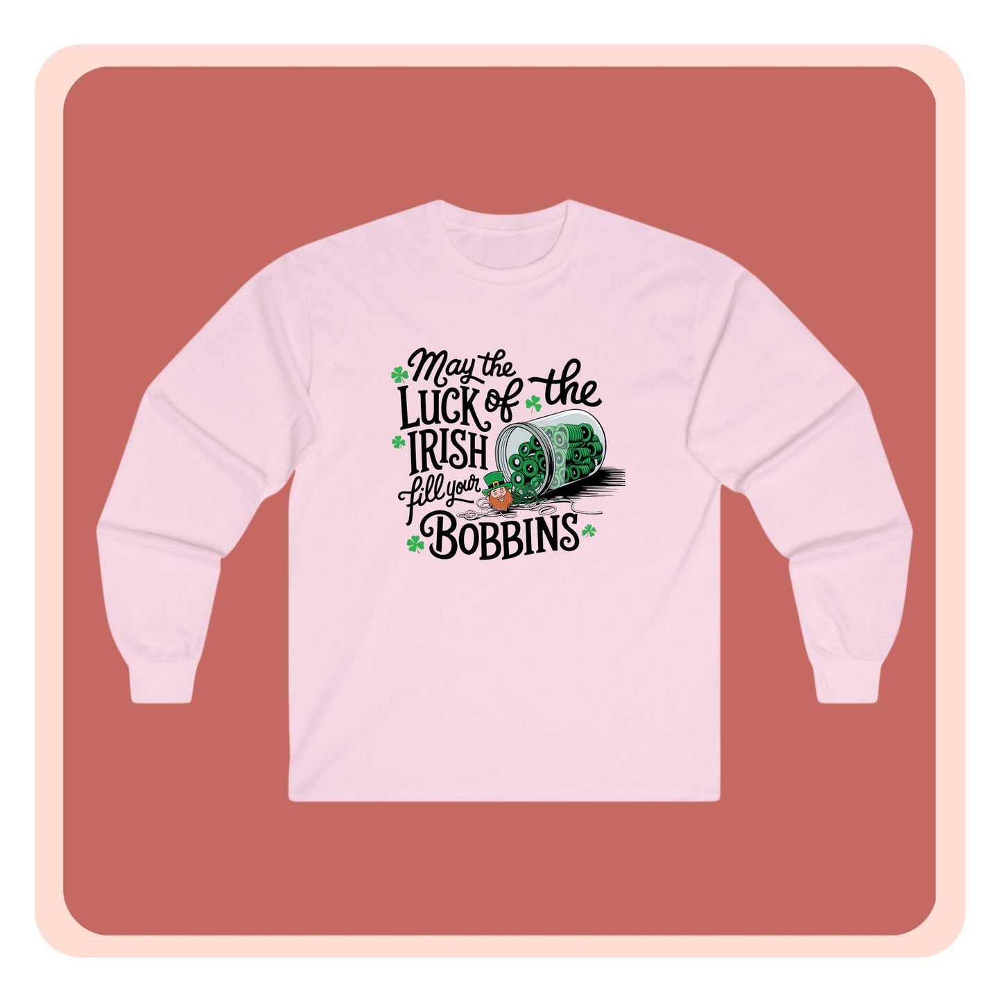 A long-sleeve t-shirt featuring a festive design with shamrocks, a spool of green thread, and the phrase 'May the Luck of the Irish Fill Your Bobbins,' perfect for quilters celebrating St. Patrick’s Day.