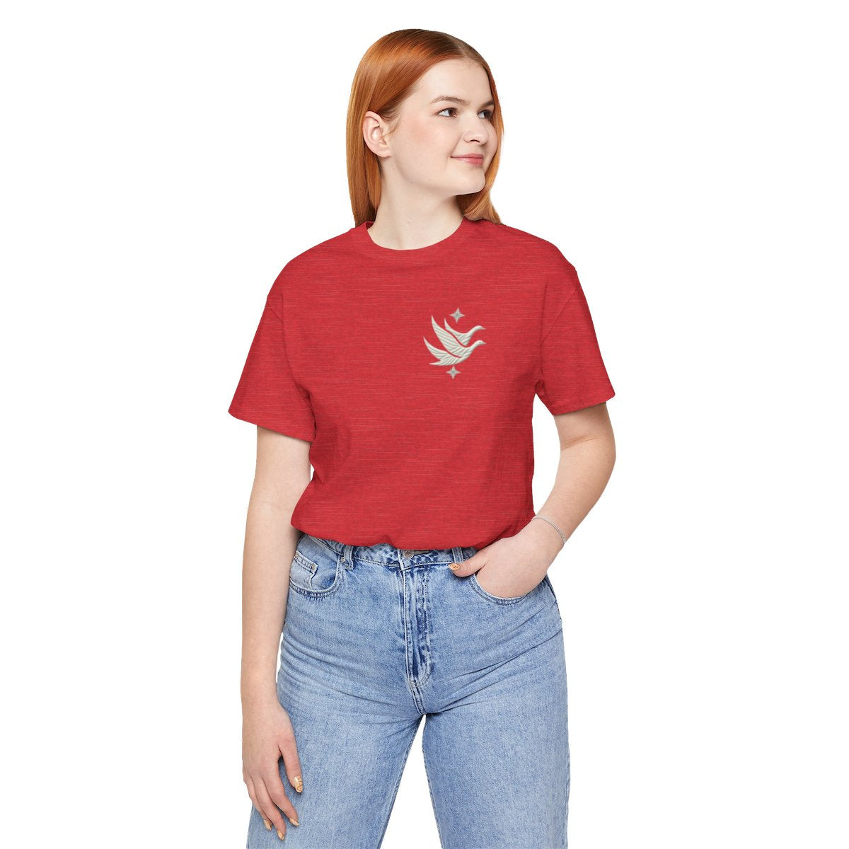 A Heather Red T-shirt featuring two stylized white geese in flight, with outstretched wings. The geese are composed of intricate geometric patterns resembling quilt stitching. Two eight-pointed stars frame the scene, one above and one below the geese, adding a celestial element to the peaceful composition.