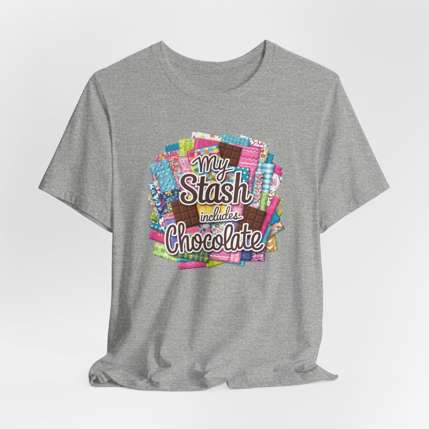 An Athletic Heather t-shirt featuring a colorful design of a fabric stash mixed with chocolate bars and the phrase 'My Stash Includes Chocolate,' perfect for quilters and chocolate lovers