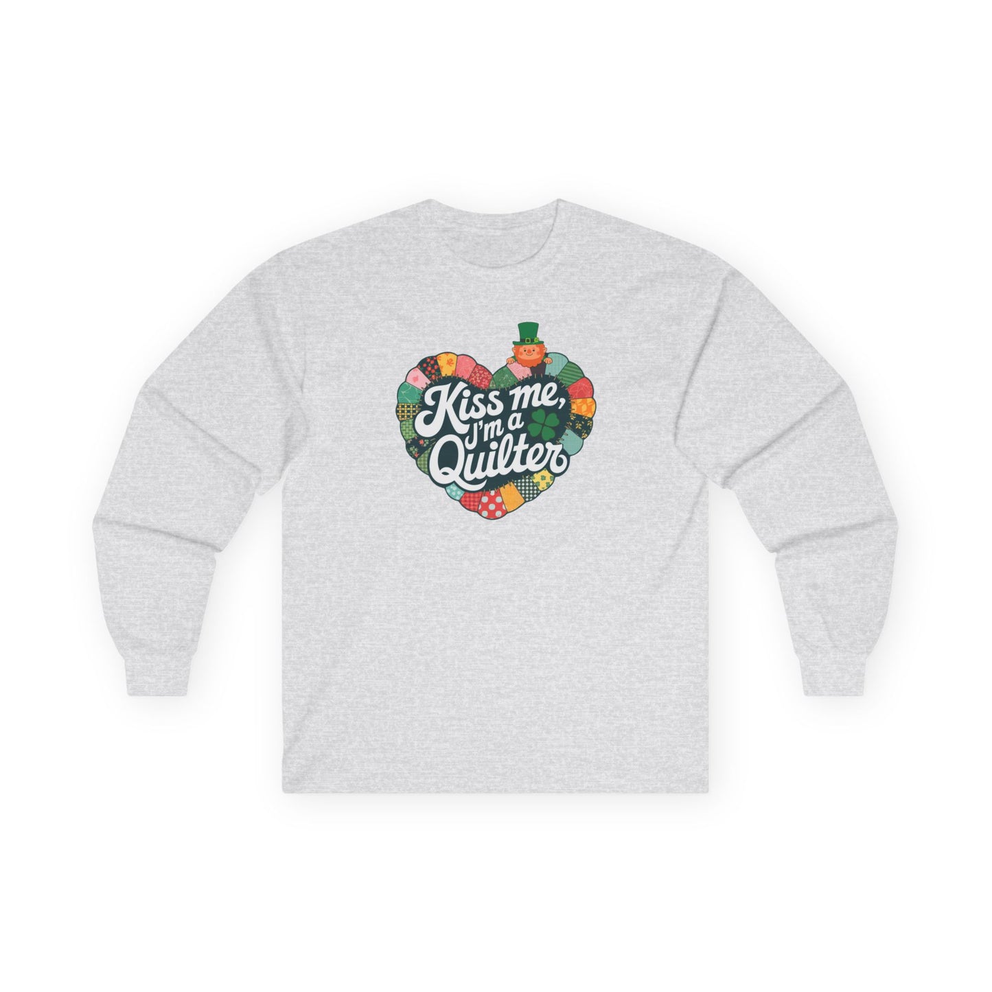 An Ash long-sleeve t-shirt featuring a heart-shaped patchwork quilt design with shamrocks, a leprechaun, and the phrase 'Kiss Me, I’m a Quilter,' perfect for St. Patrick’s Day quilting fun.