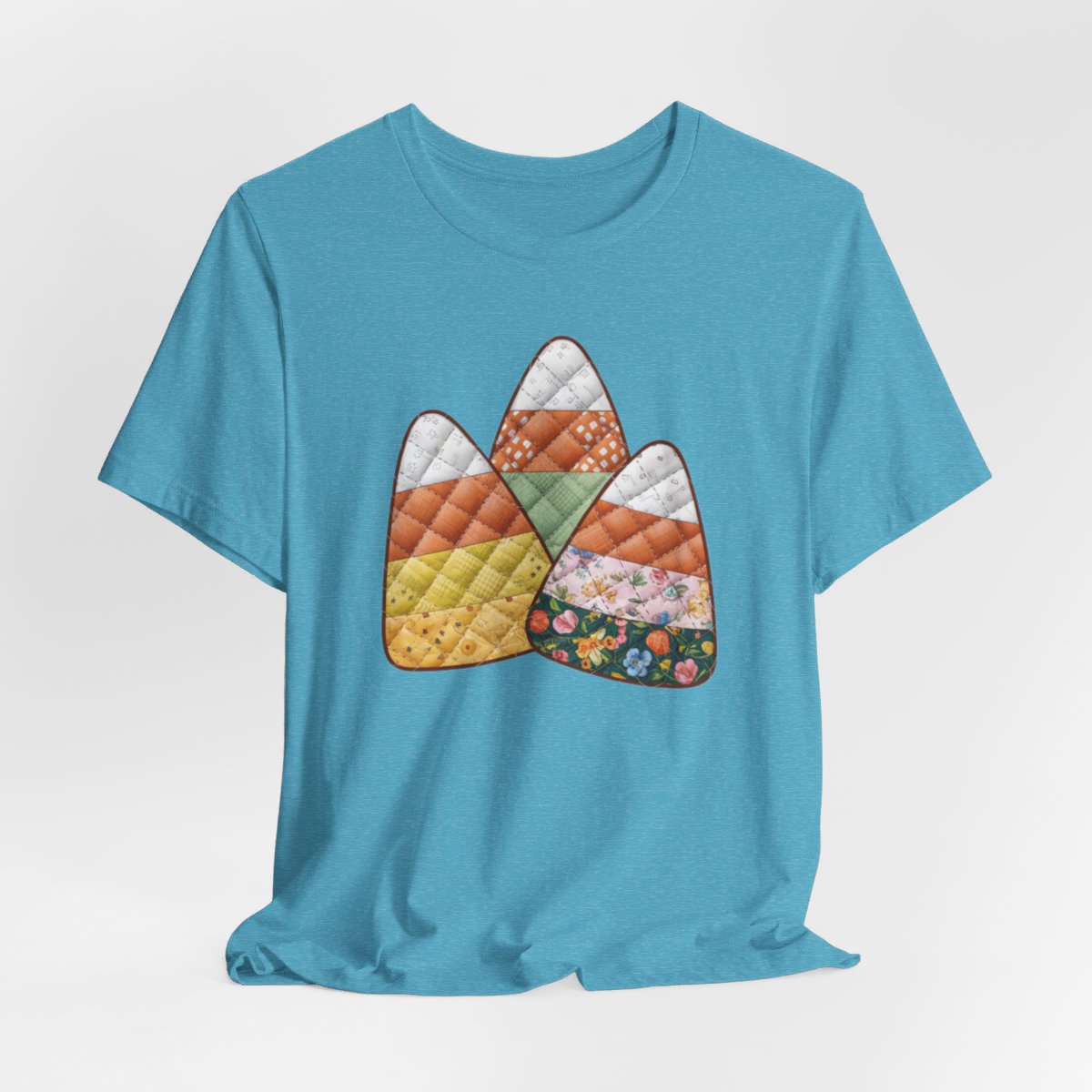 A Heather Aqua Halloween Quilting T-Shirt featuring three large candy corn shapes made of quilted fabrics with various patterns. Each candy corn section features different quilting motifs in autumn colors. Playful take on Halloween candy and quilting craft.